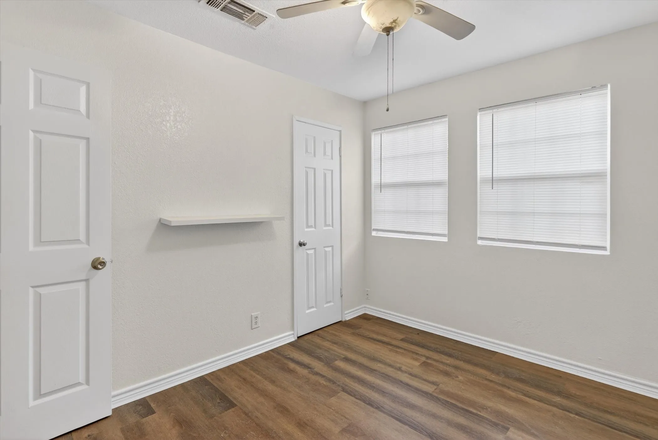 Interior room featuring wood-finish flooring, two windows with blinds, a ceiling fan, and white trim throughout