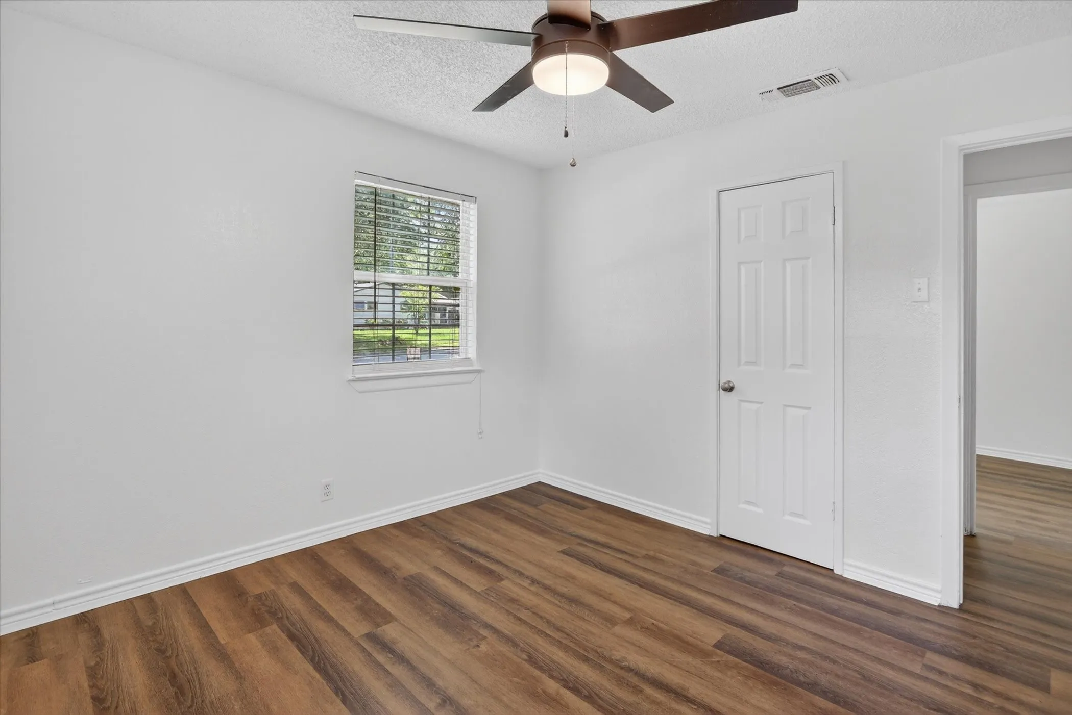 Room with wood-finish flooring, a ceiling fan with integrated lighting, a multi-pane window with horizontal blinds, and a white paneled door