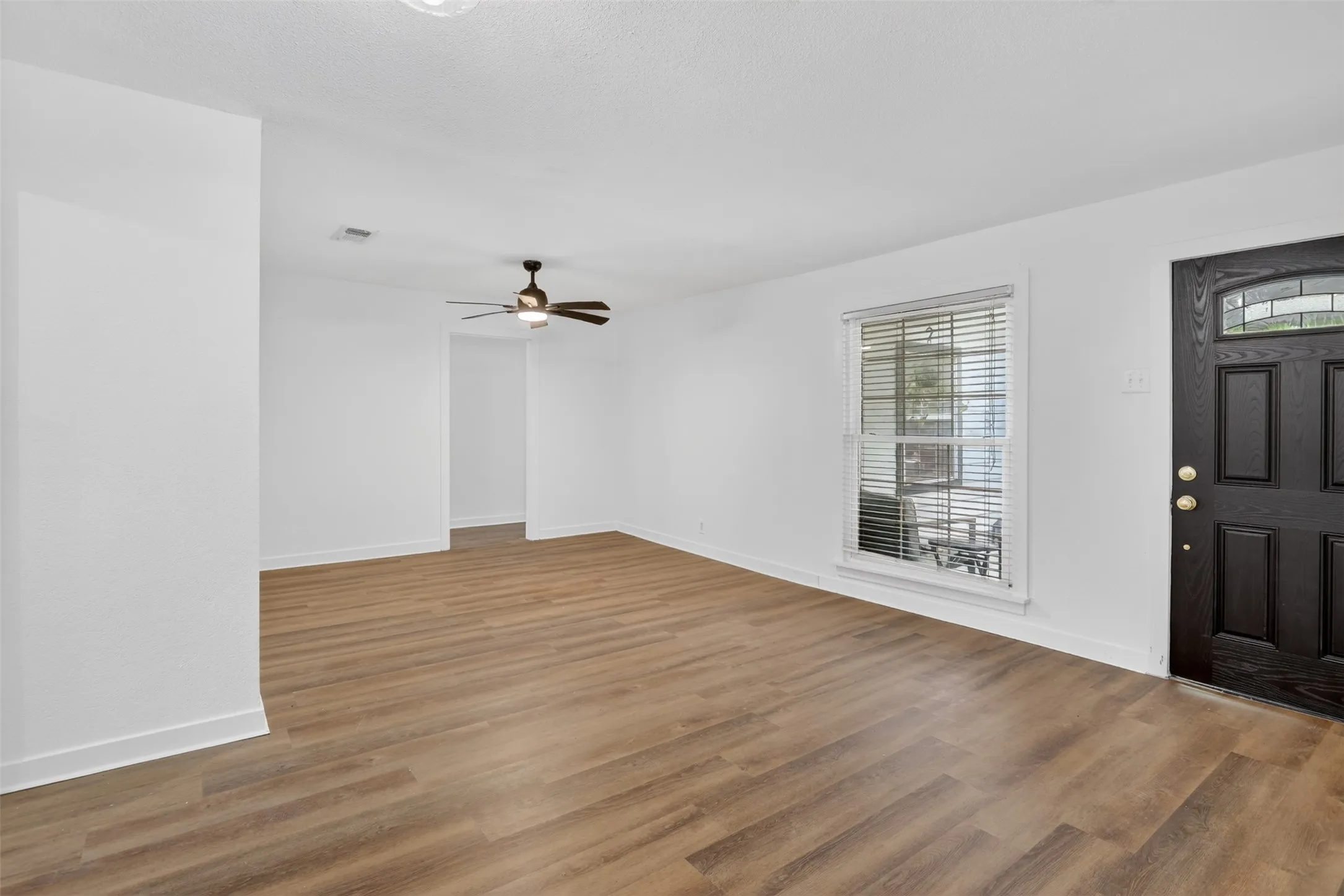 Spacious livingroom featuring wood-finish flooring, white baseboards, and a modern ceiling fan