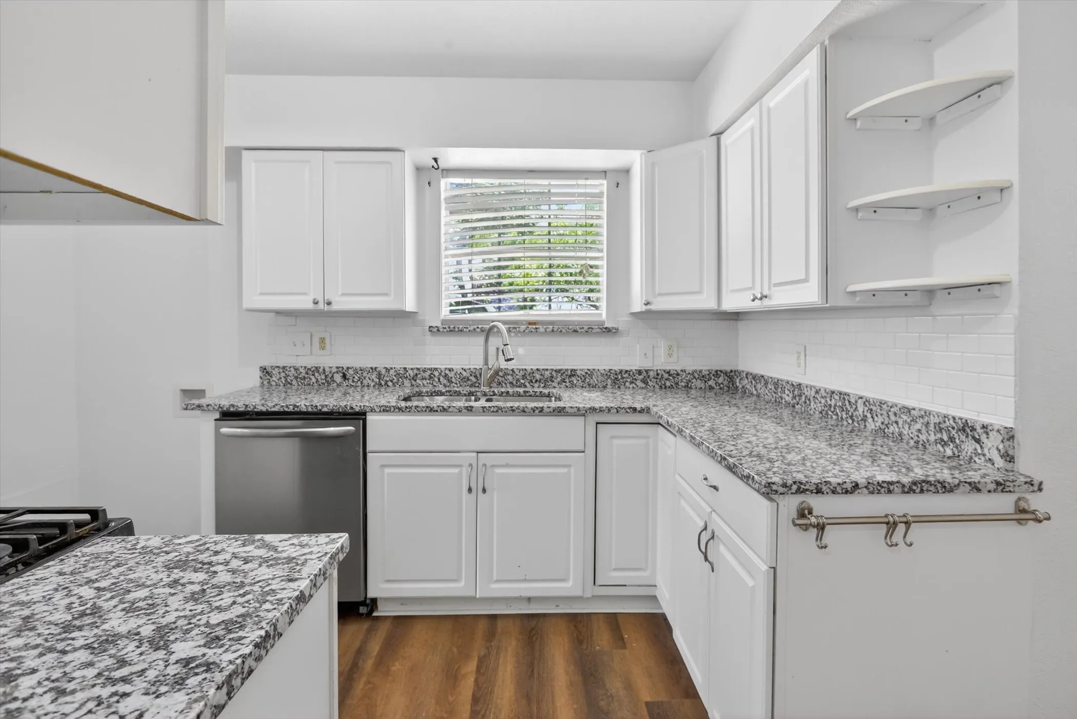 Kitchen featuring white shaker-style cabinetry, patterned countertops, a stainless steel dishwasher, and wood-finish flooring