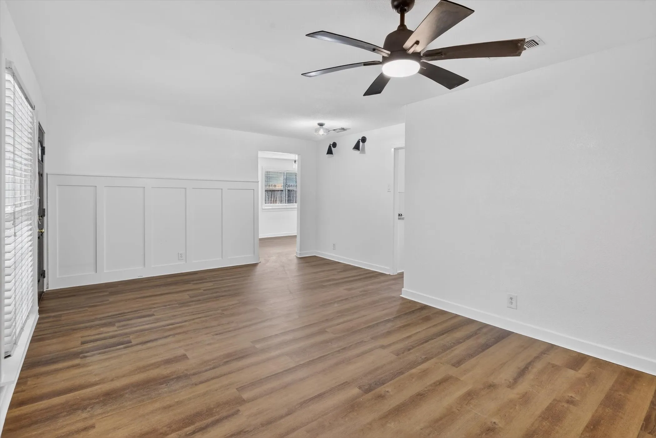 Spacious livingroom featuring wood-finish flooring, crisp white walls, and wainscoting