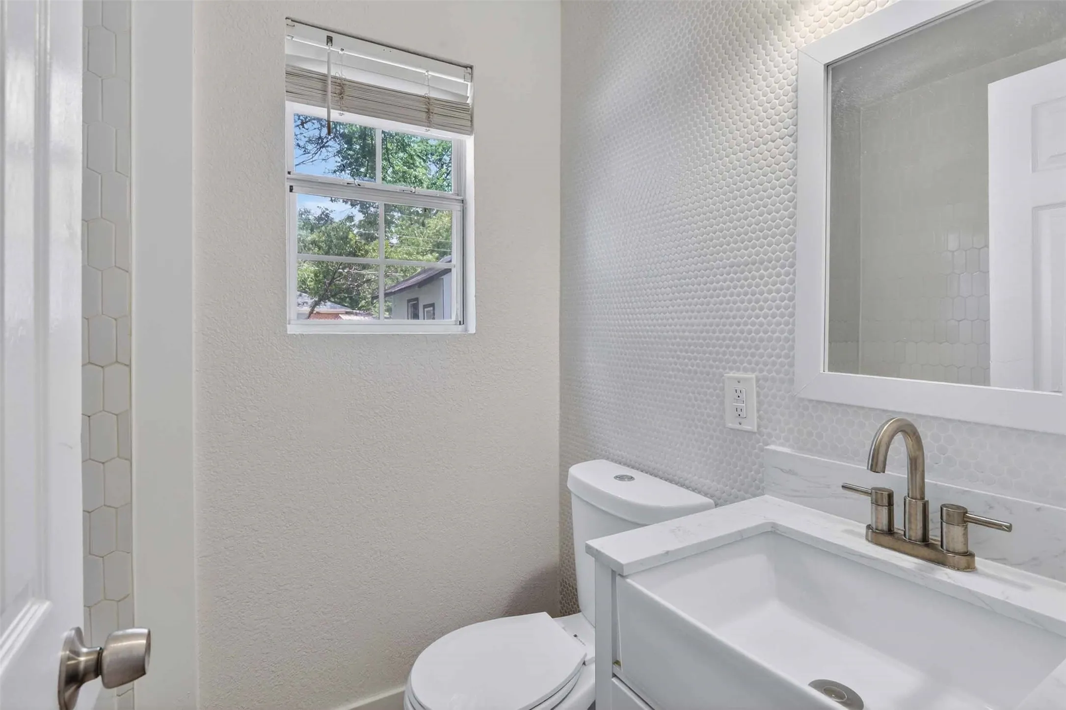 Contemporary bathroom featuring a white vanity with integrated sink, brushed nickel faucet, and a wall of penny tile