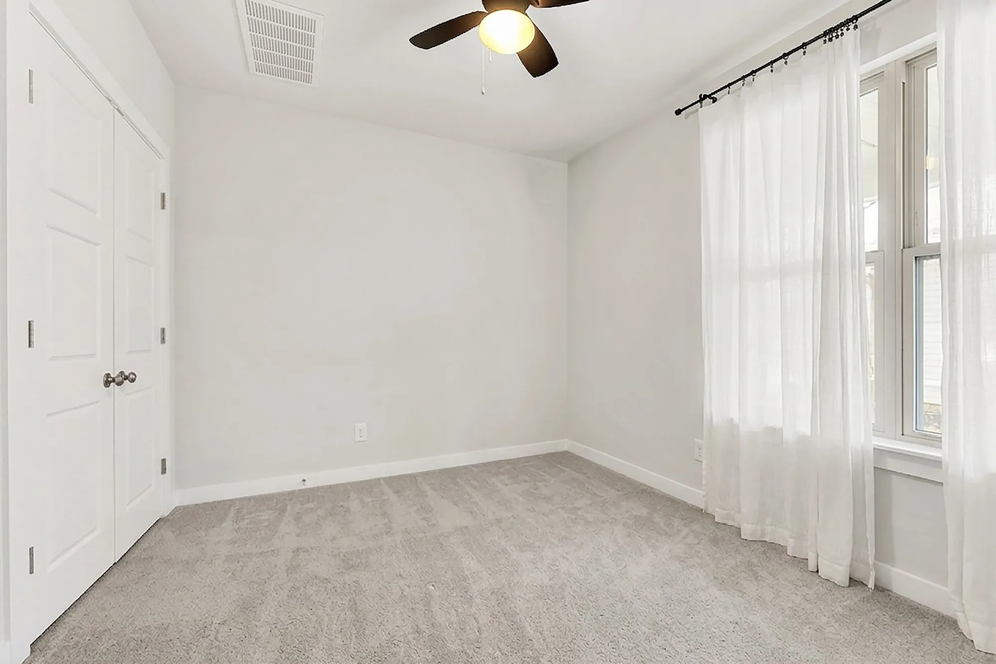 Plush carpeting, ceiling fan with integrated lighting, white paneled doors, and a double window with curtain rod