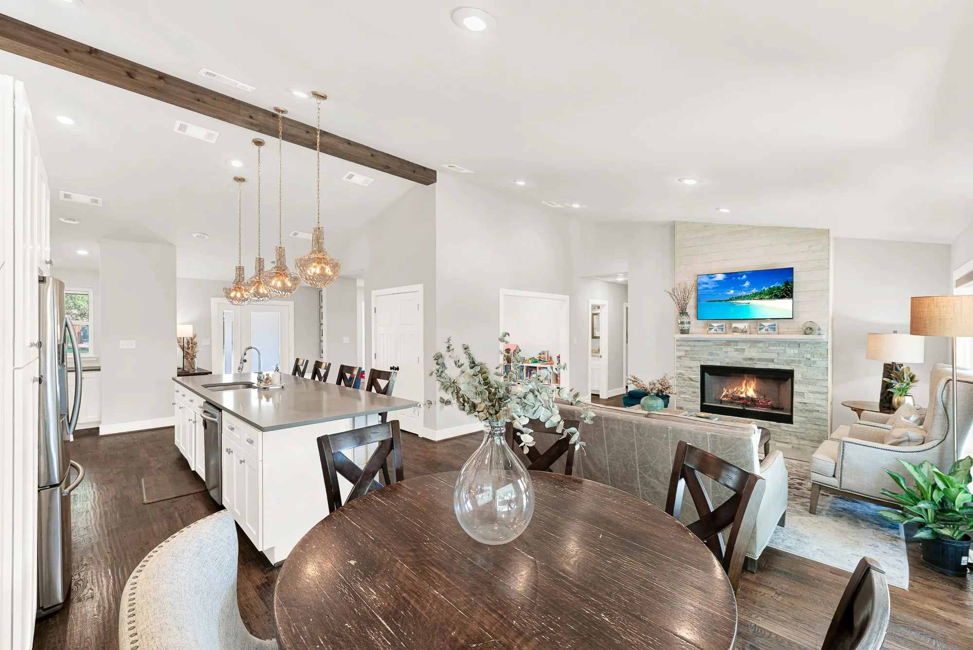 Expansive open-concept living area featuring a stone fireplace, wood-finish flooring, and vaulted ceilings
