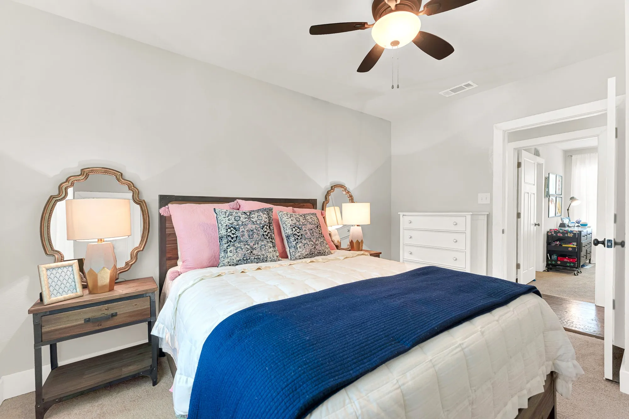 Ceiling fan with integrated lighting, wood-finish headboard, built-in dresser, and an open doorway