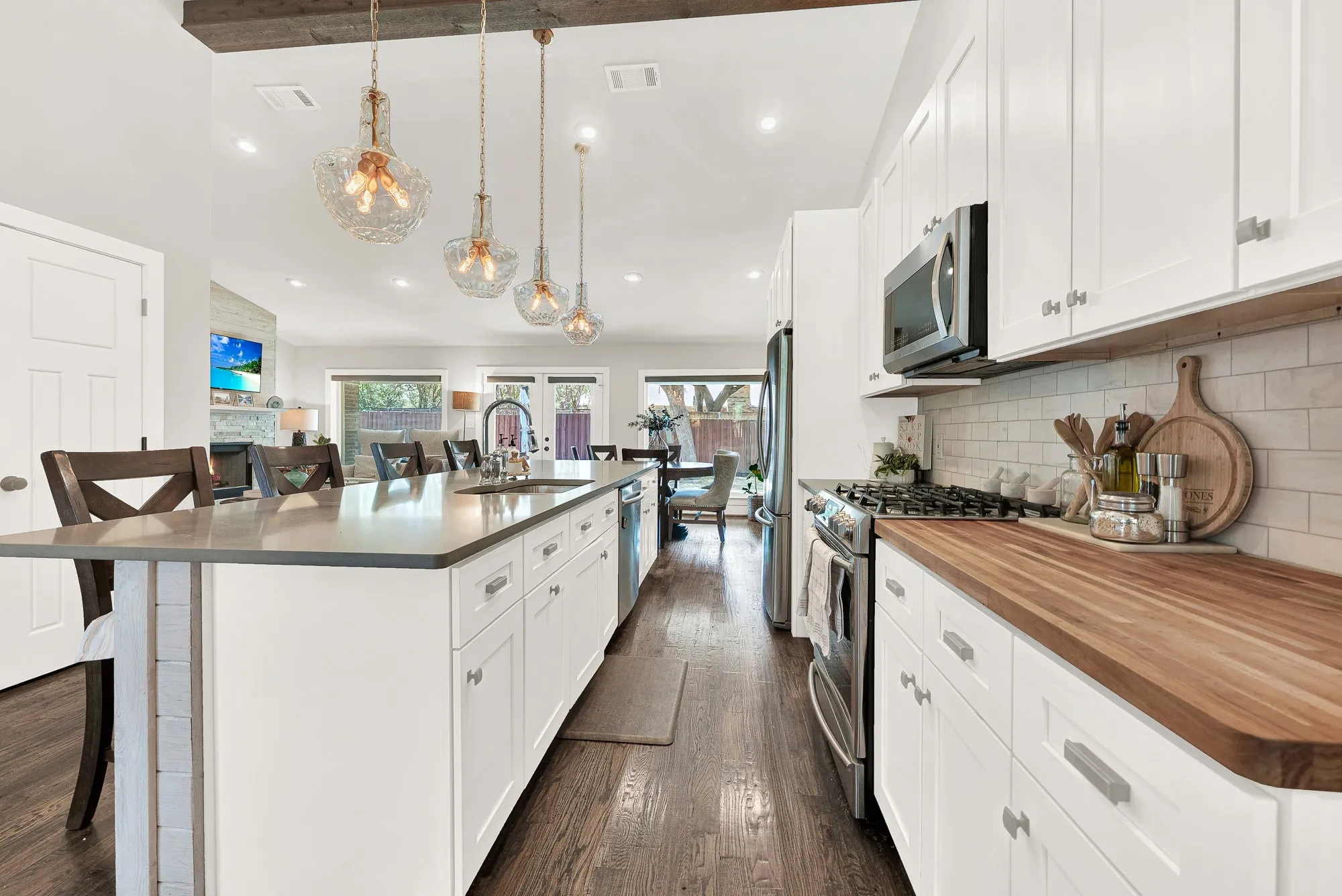 Spacious kitchen featuring an extended island with a built-in sink, white shaker cabinetry, stainless steel appliances, and wood-finish countertops