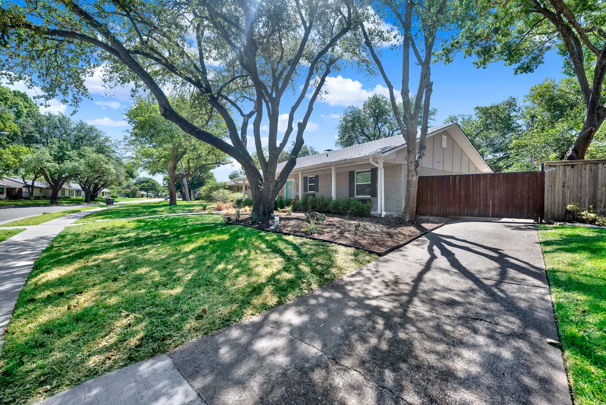 Mid-century modern exterior featuring a gabled roof, a private wooden fence, and an asphalt driveway