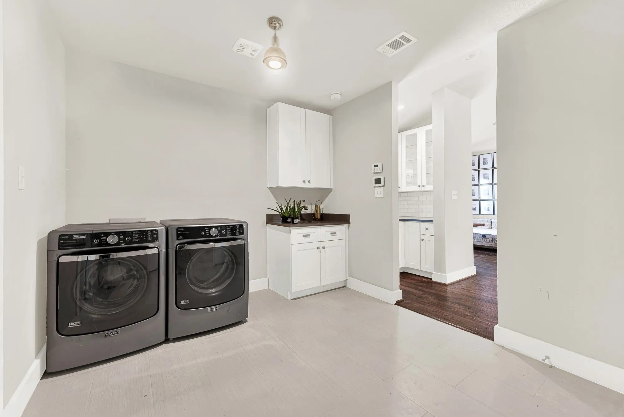 Laundry area featuring light wood-finish flooring, white cabinetry with a dark countertop, and an overhead light fixture