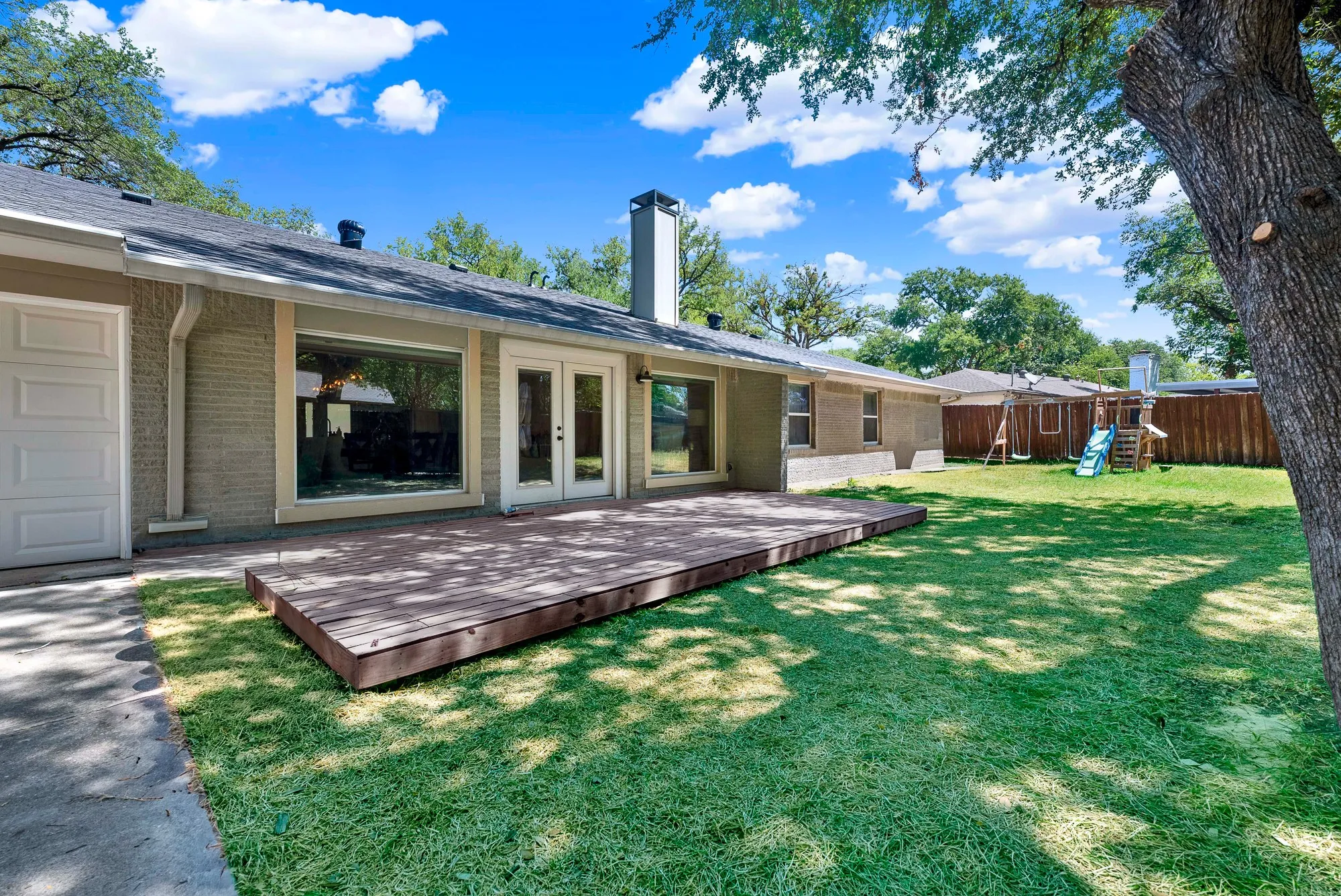 Expansive backyard featuring a large wood deck, extensive green lawn, and mature trees