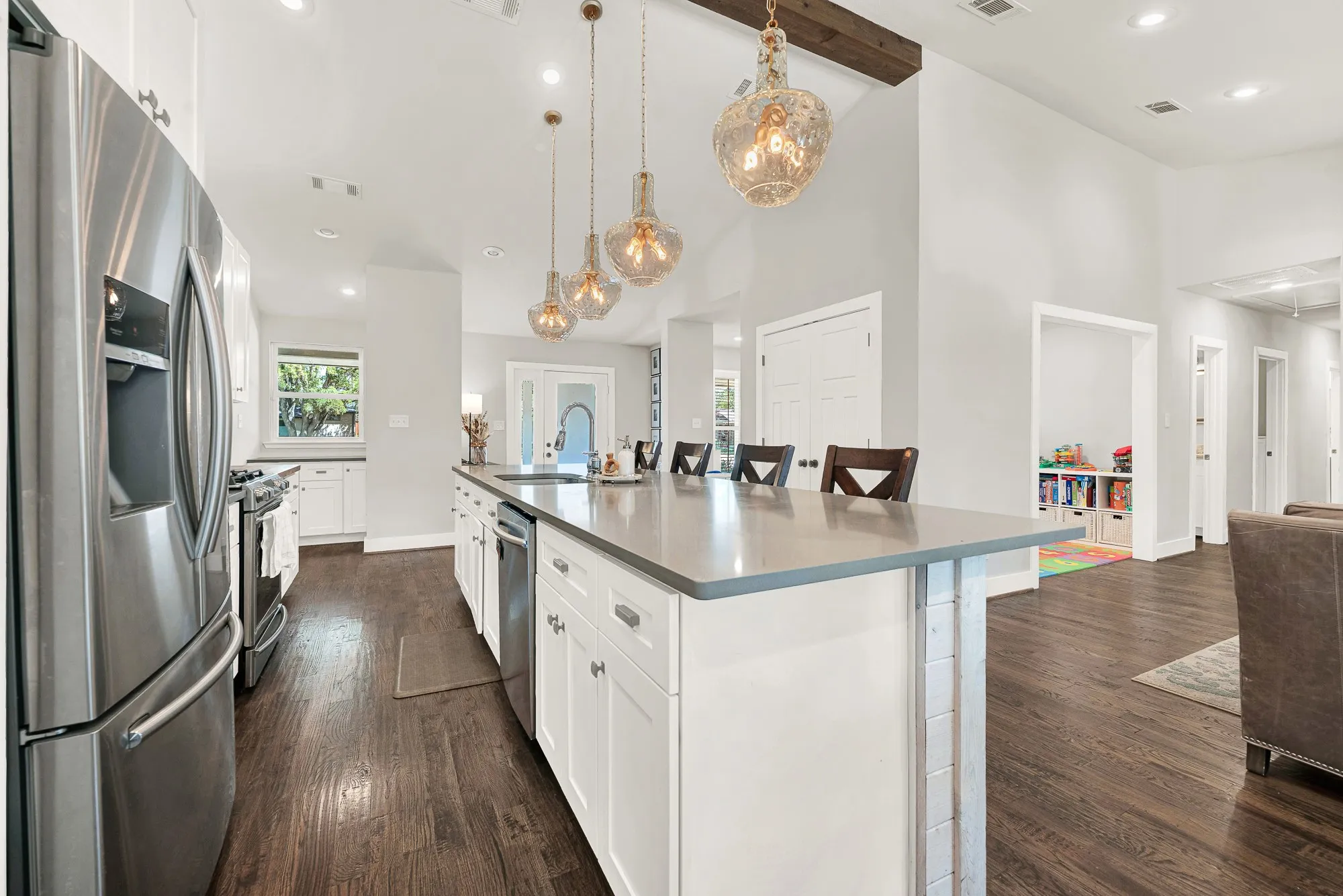 Kitchen featuring a central island with countertop seating, stainless steel appliances, wood-finish flooring, white cabinetry, and pendant lighting