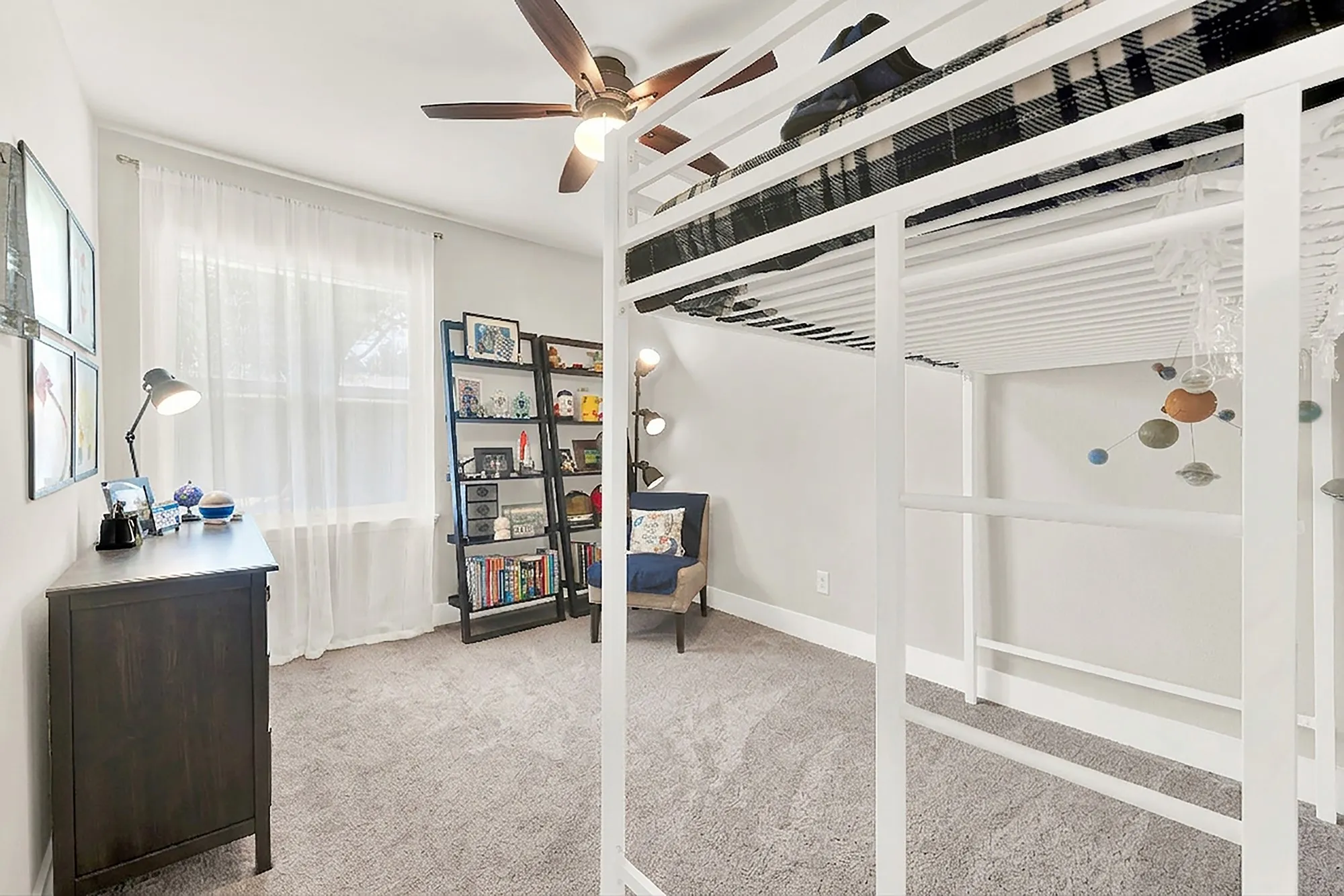 Carpeted room featuring a ceiling fan, a window with sheer curtains, and a built-in metal loft bed frame
