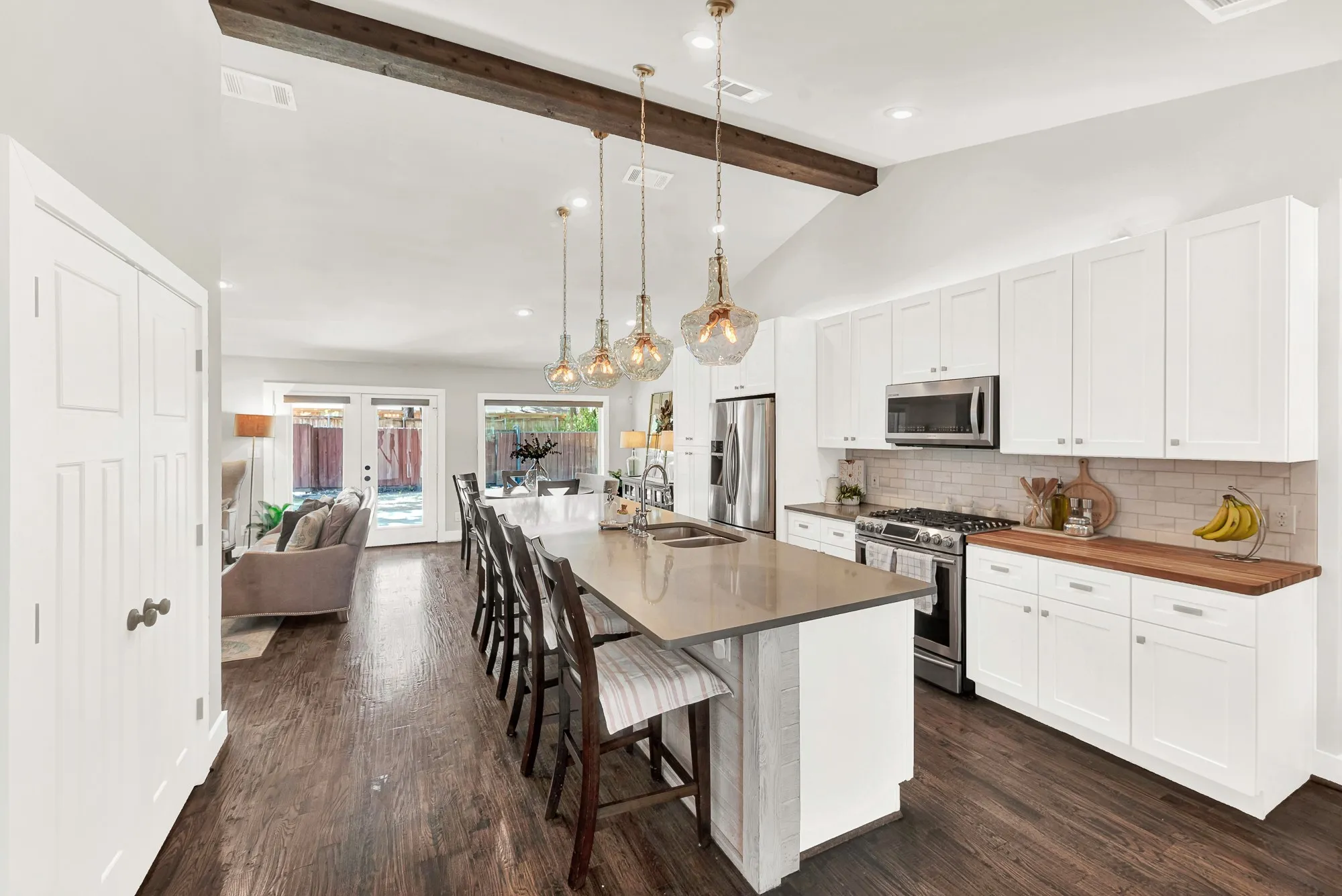 Kitchen featuring a large island with seating, pendant lighting, wood-finish flooring, white cabinetry, and stainless steel appliances