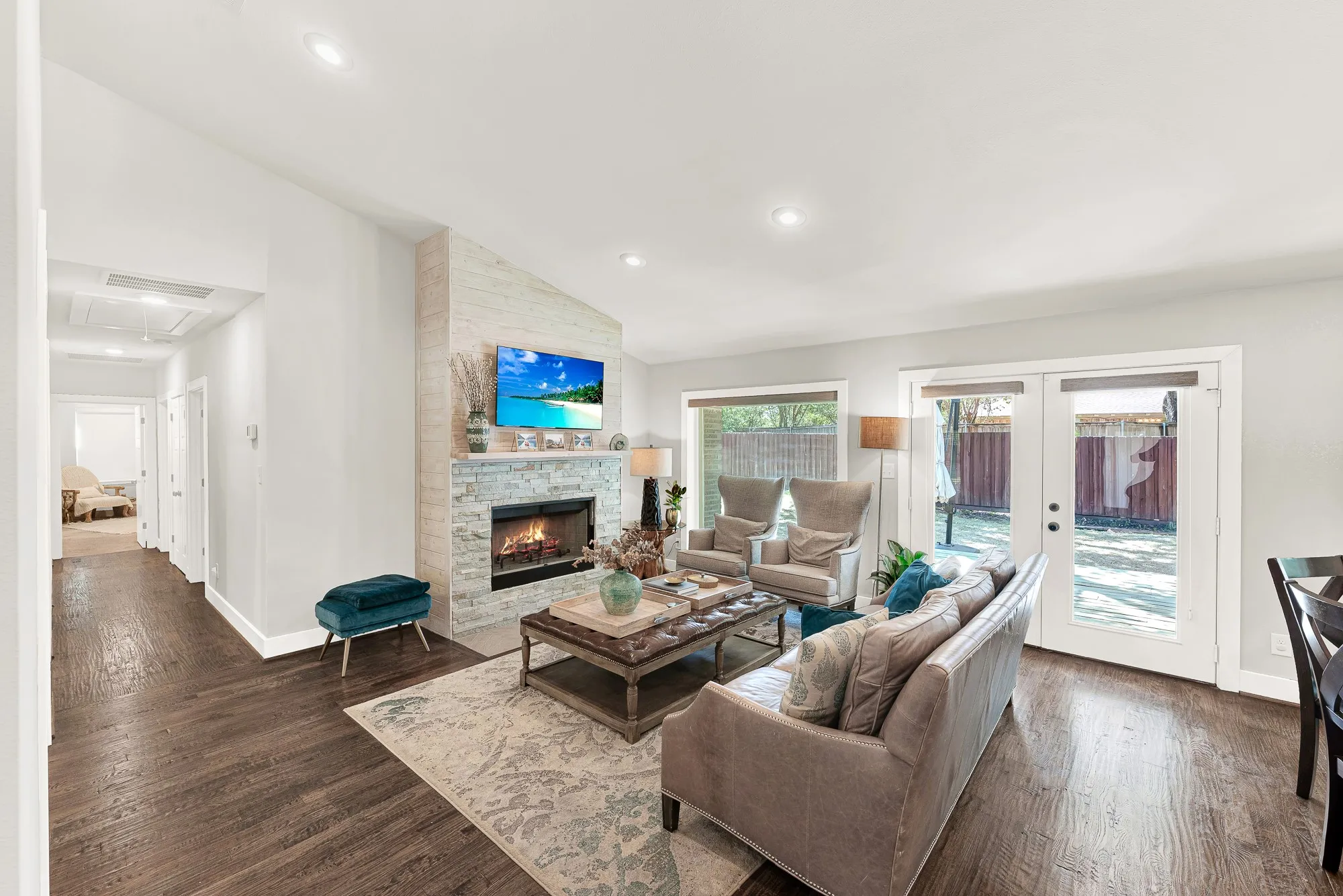 Living area featuring wood-finish flooring, a stone-clad fireplace with a mantel, recessed lighting, and French doors leading to an outdoor area