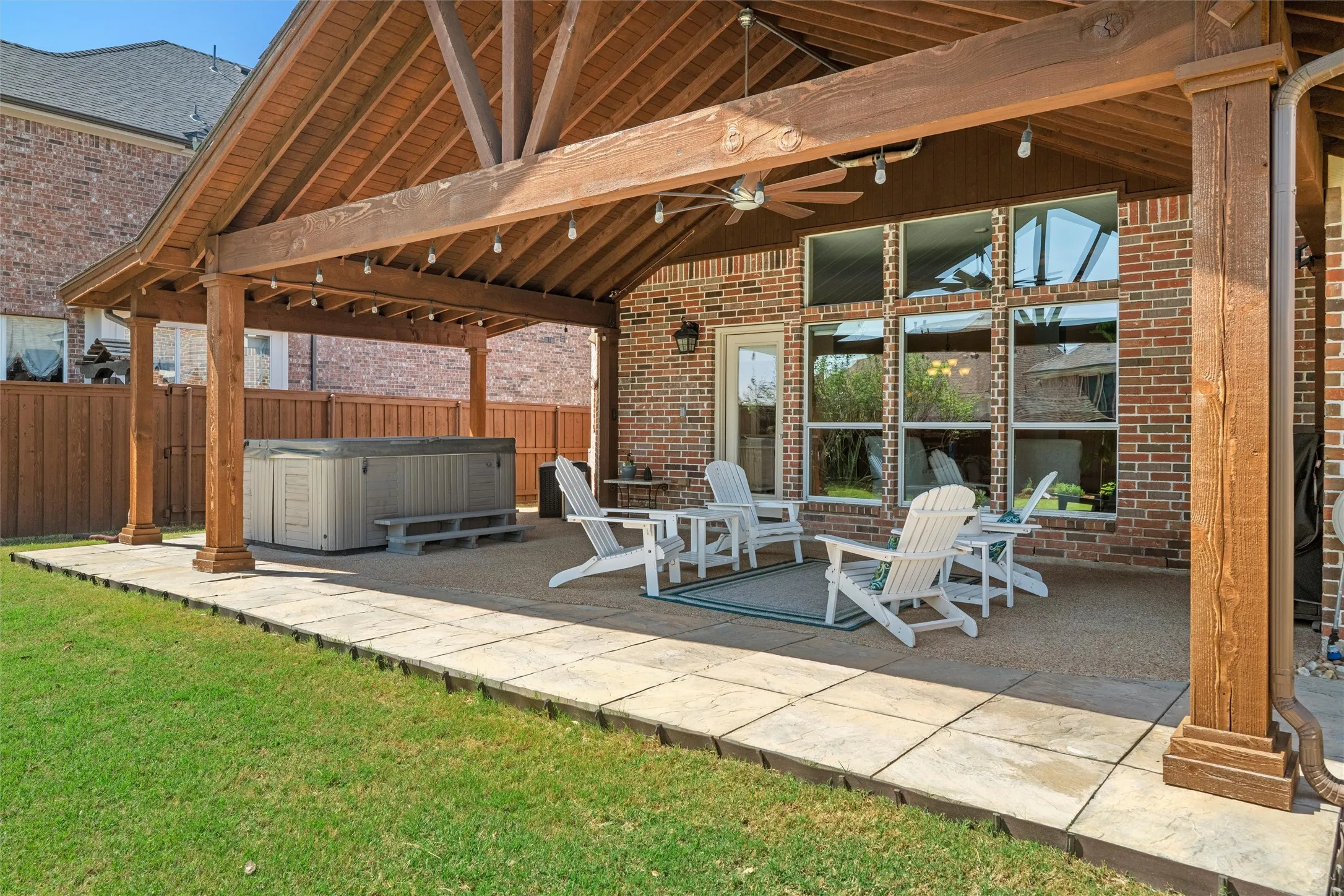 Expansive covered patio with exposed wood beams, ceiling fan, string lighting, and a built-in hot tub