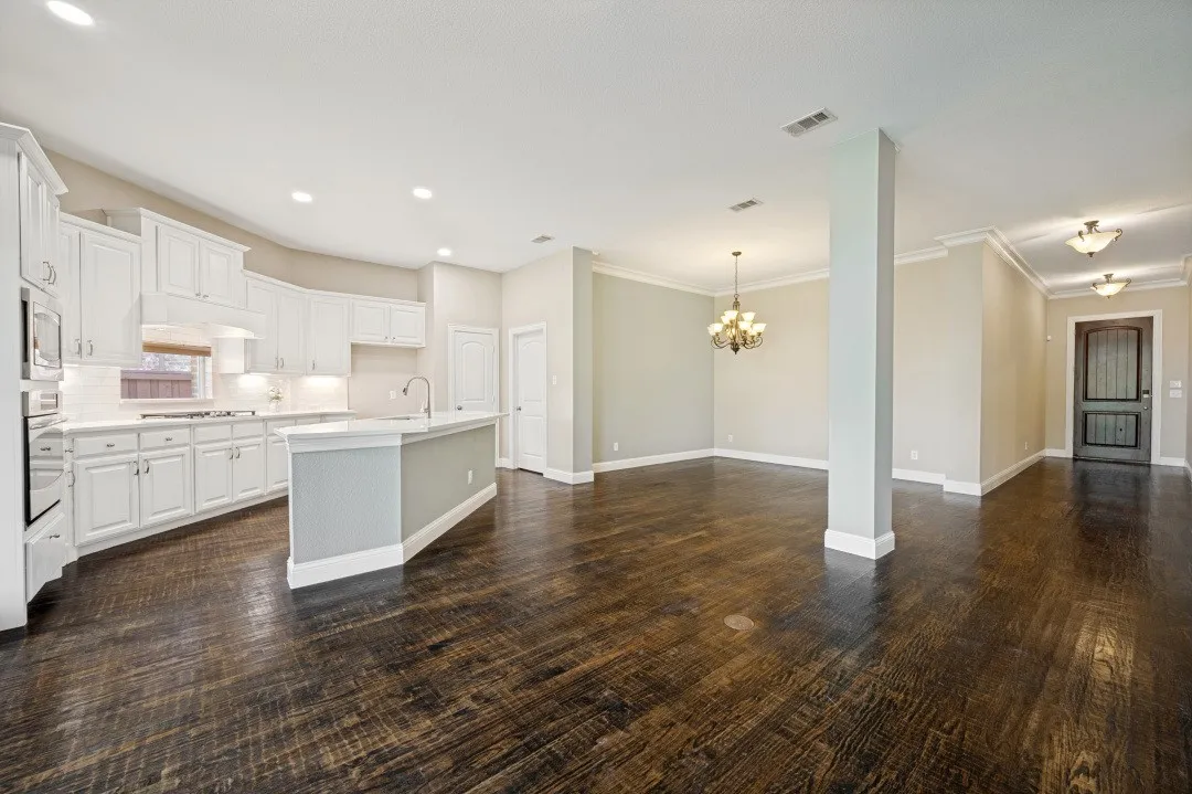 Open-concept living space with dark wood-finish flooring, white kitchen cabinetry, a central kitchen island, recessed lighting, and a decorative chandelier