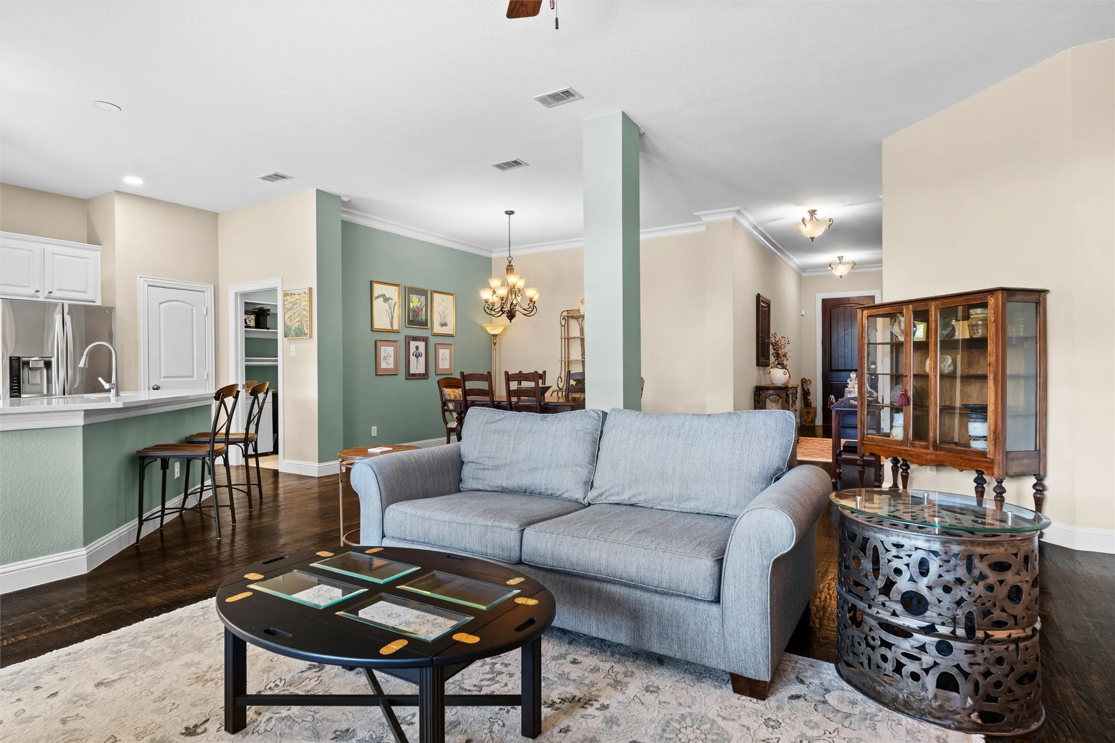 Open-concept living space featuring a light blue upholstered sofa, dark wood-finish flooring throughout, and architectural columns defining the layout