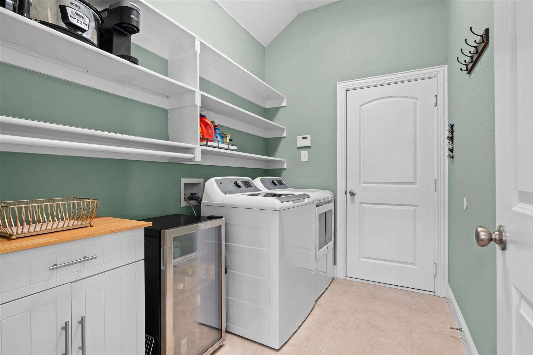 Built-in shelving, wood-finish countertop, lower cabinetry with stainless steel pulls, and light-toned tile flooring