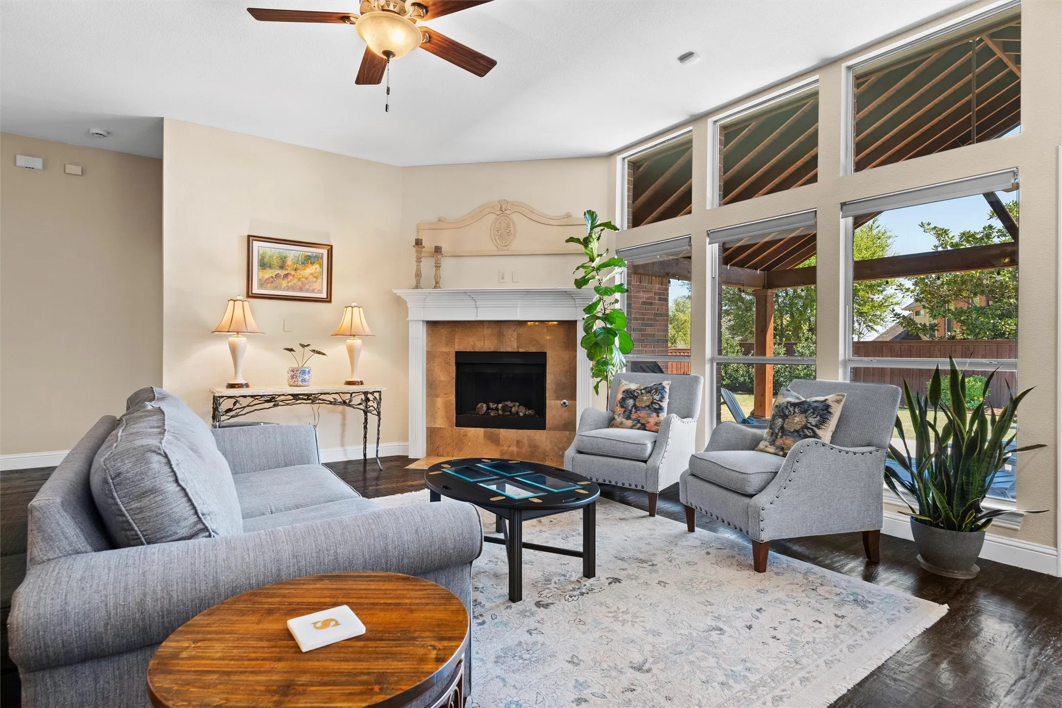 Vaulted ceiling with a ceiling fan, fireplace with a tile surround and decorative mantle, large picture windows, dark wood-finish flooring, and recessed lighting
