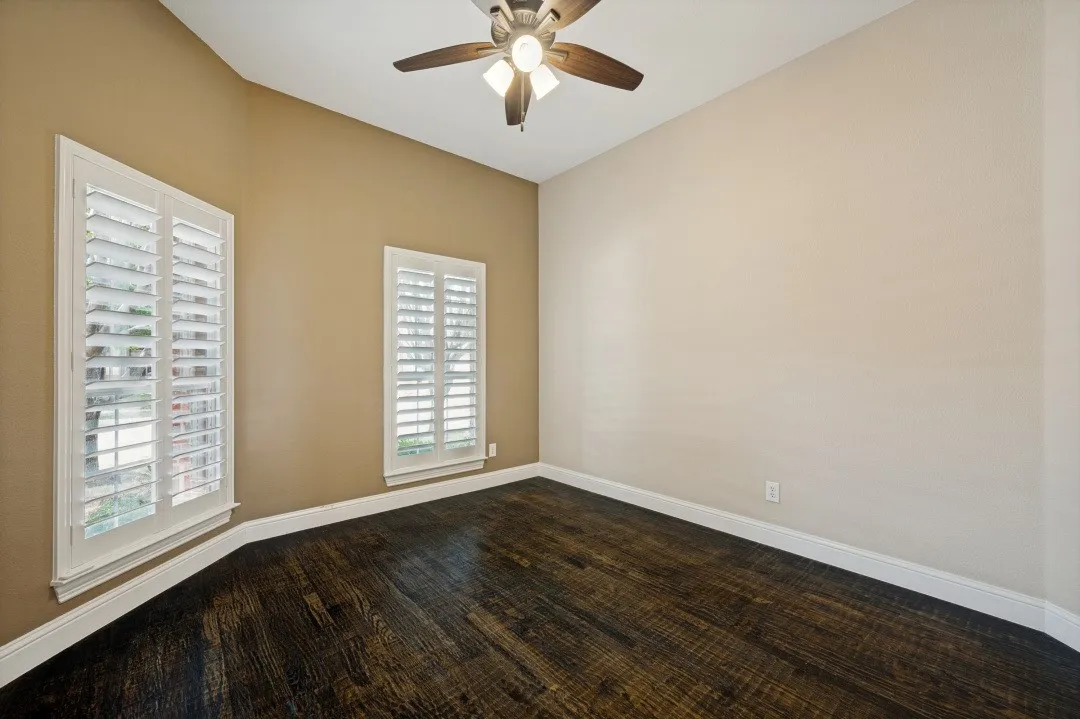 Dark wood-finish flooring, white plantation shutters, angled ceiling, ceiling fan, and white baseboards