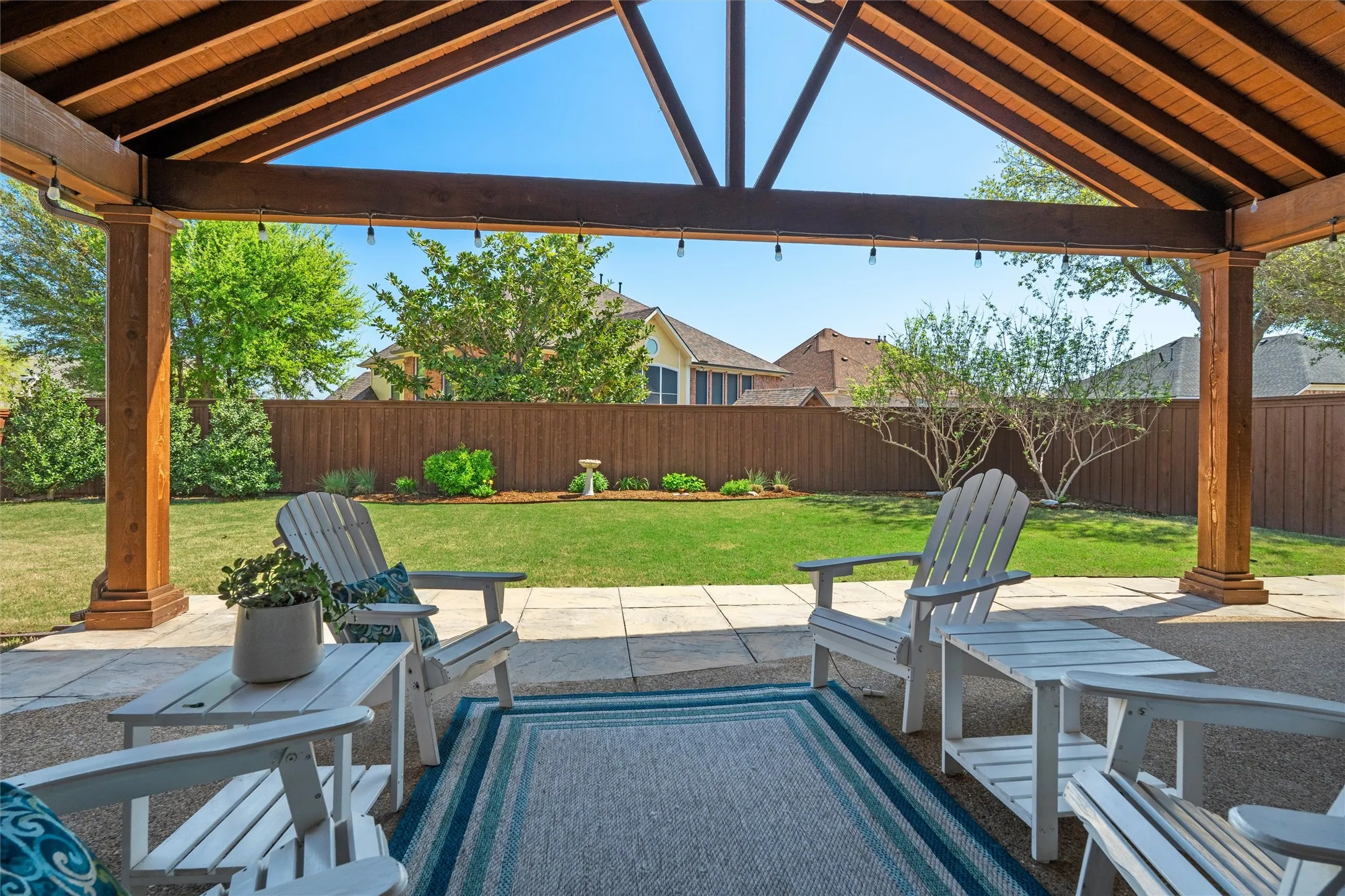 Covered patio with a high vaulted ceiling, exposed wood beams, concrete paver flooring, and string lighting