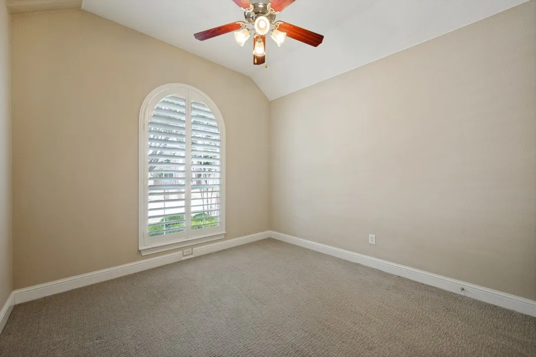 Arched window with plantation shutters, vaulted ceiling, ceiling fan with light fixture, neutral carpet, and light-toned walls