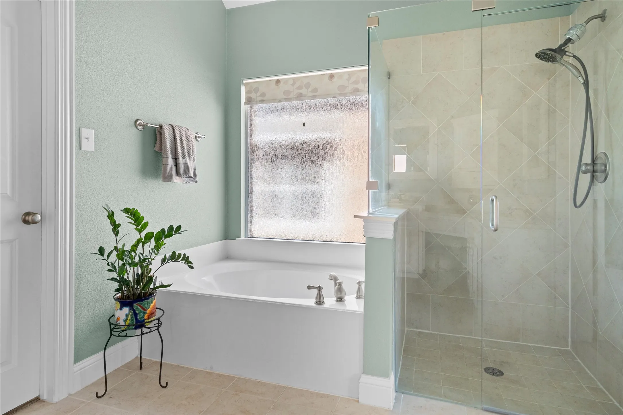 Soaking tub with deck-mounted fixtures, glass-enclosed shower with tile surround, and frosted window