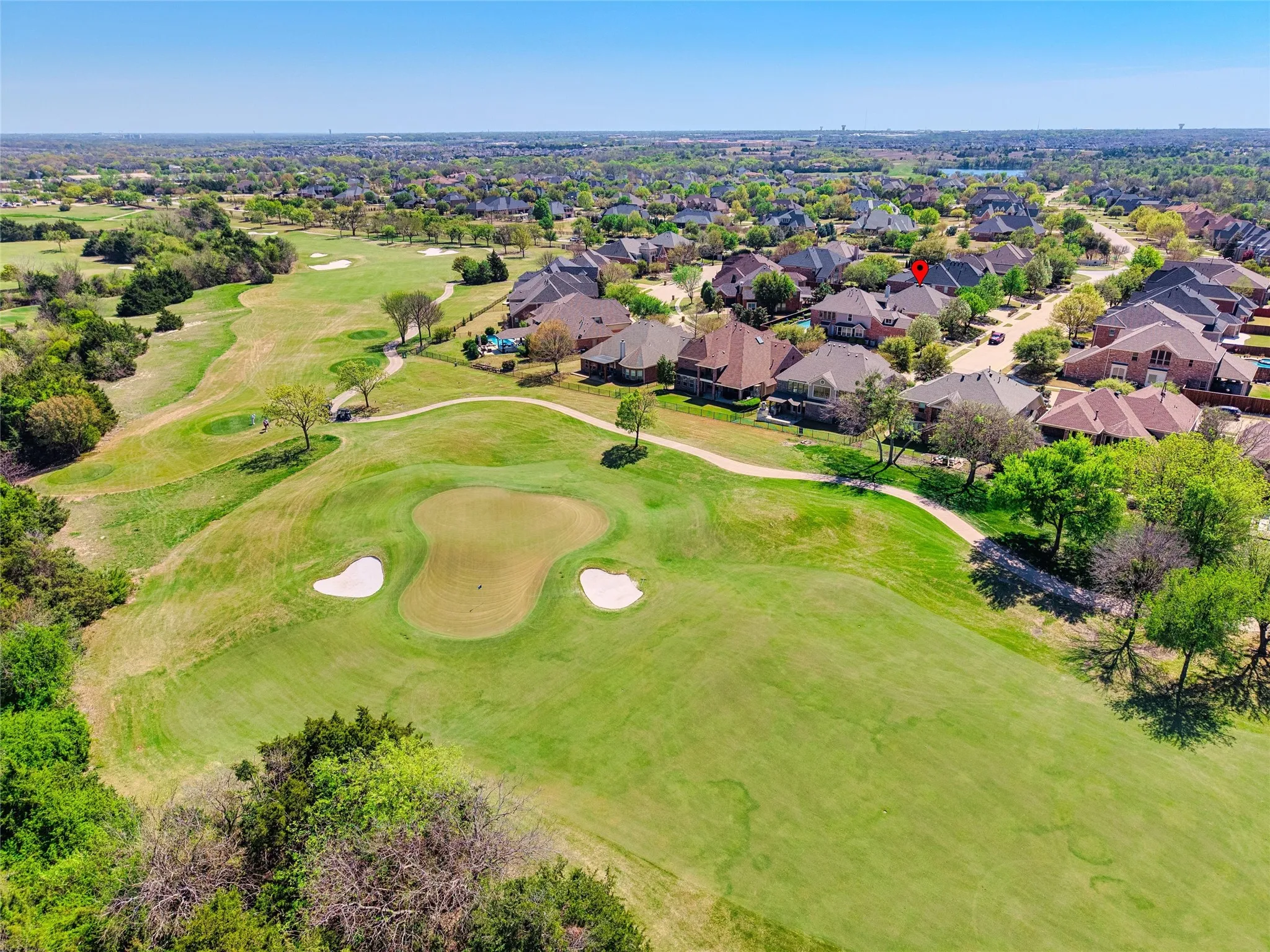 Expansive green spaces with manicured golf course greens and sand traps, surrounded by mature trees and residential properties