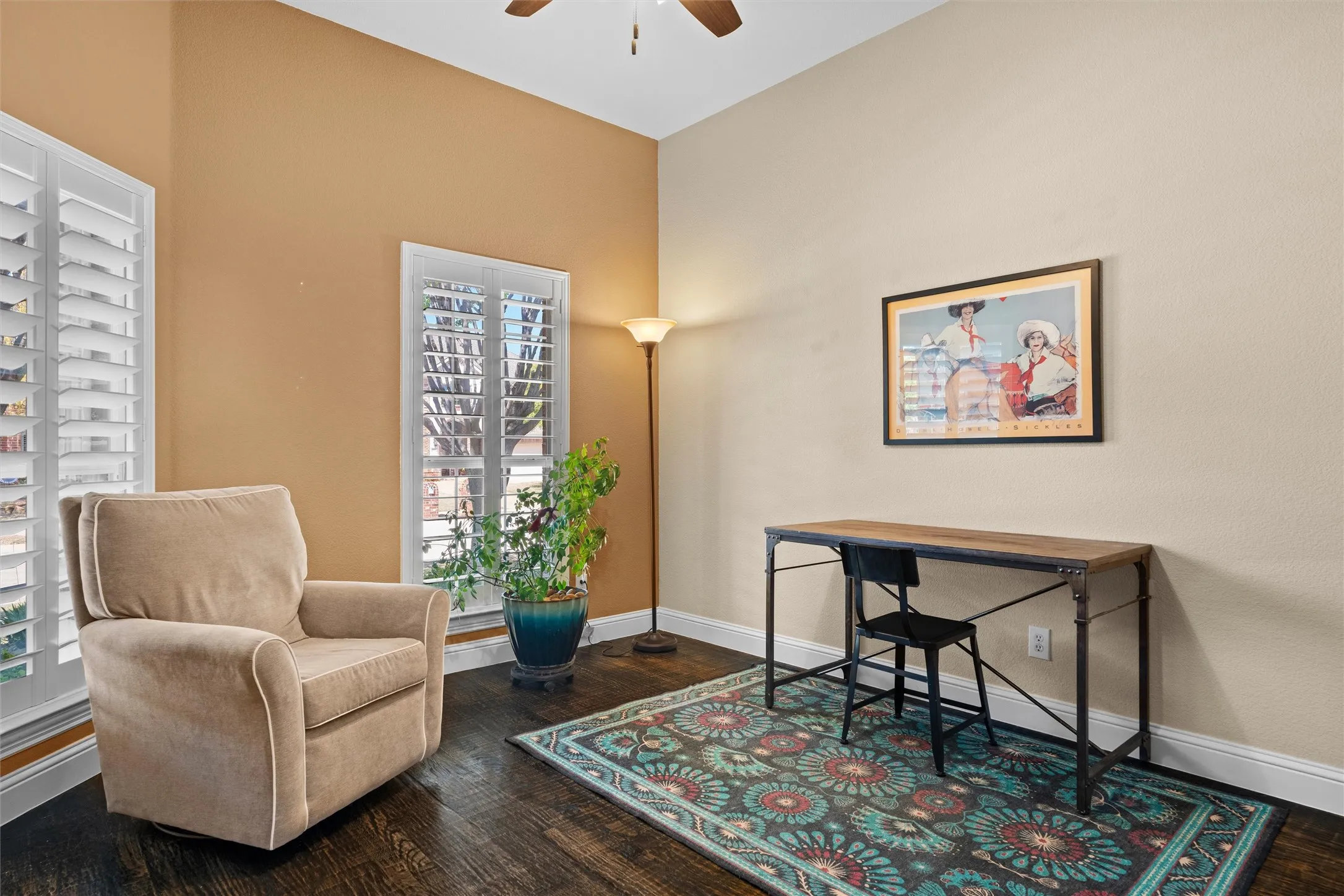 Room featuring wood-finish flooring, two windows with white plantation shutters, and a ceiling fan