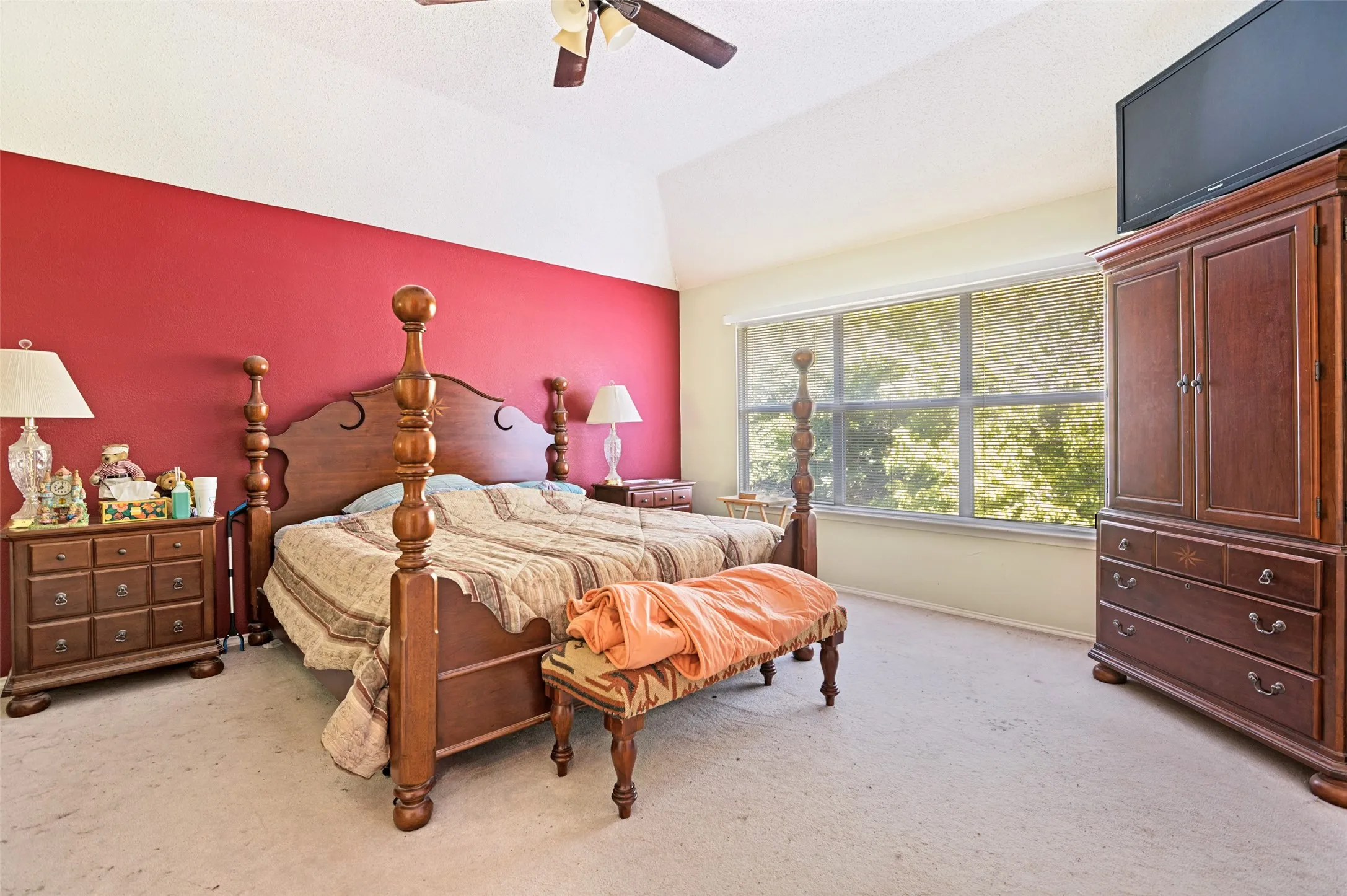 Primary Bedroom with Vaulted ceiling with ceiling fan, large window with roller shade, and light-colored carpeting