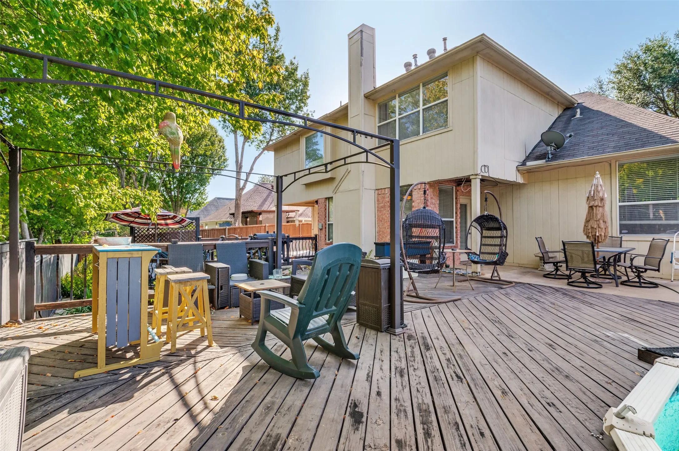 Multi-level wood deck with a metal pergola structure, brick and siding exterior, and multiple windows