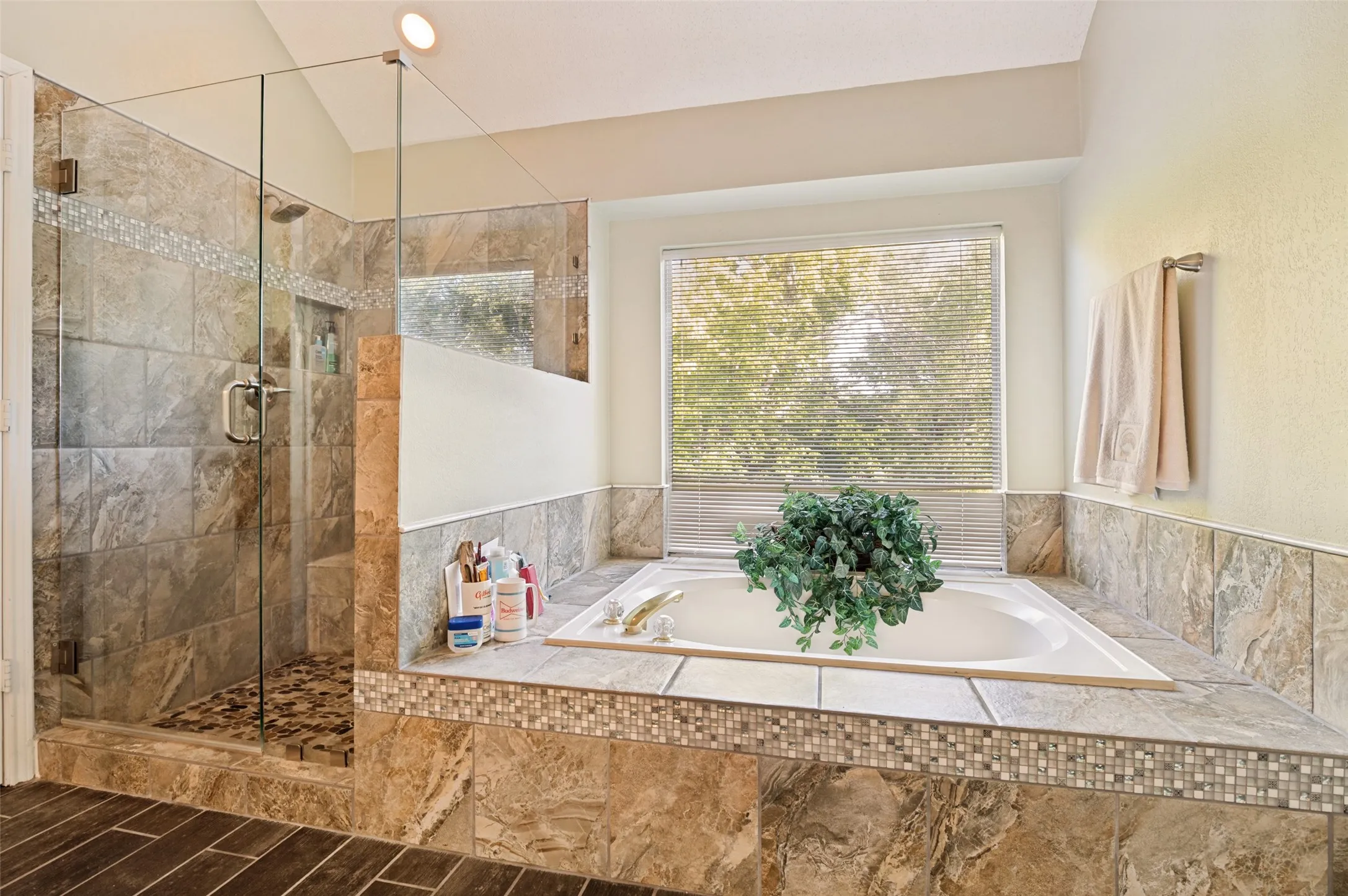 Spacious Primary bathroom featuring a built-in soaking tub, glass-enclosed shower with tile surround, and wood-finish flooring.