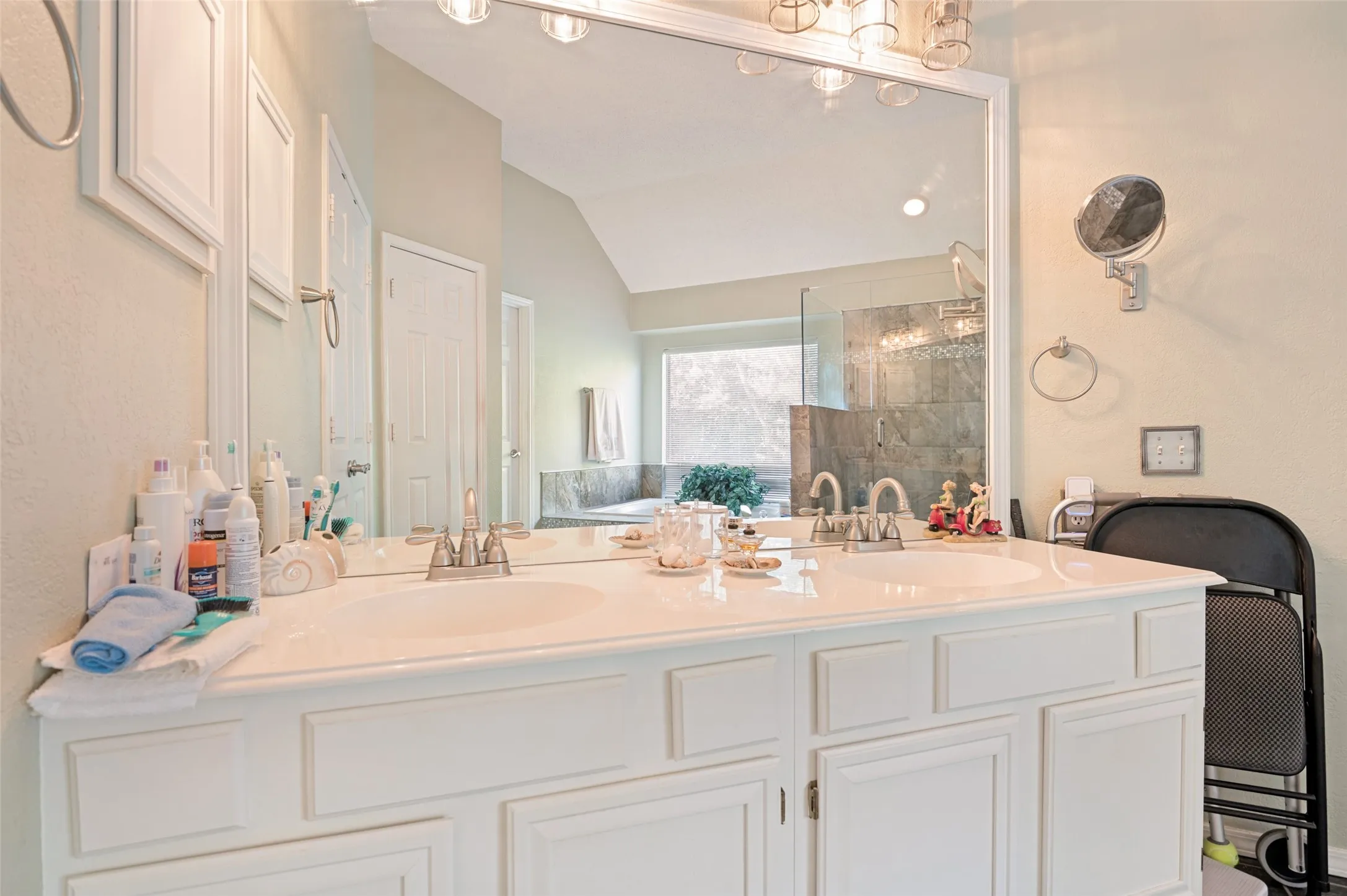 Spa-inspired primary bathroom featuring a dual-sink vanity with raised-panel cabinetry, light quartz countertop, and polished brass hardware