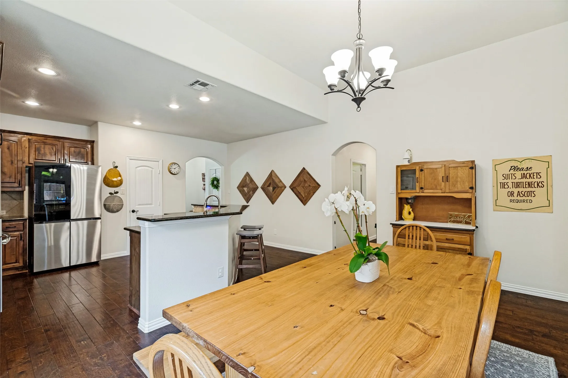 Open-concept living area featuring rich wood-finish flooring, a kitchen island with a dark countertop, white walls, and an arched doorway