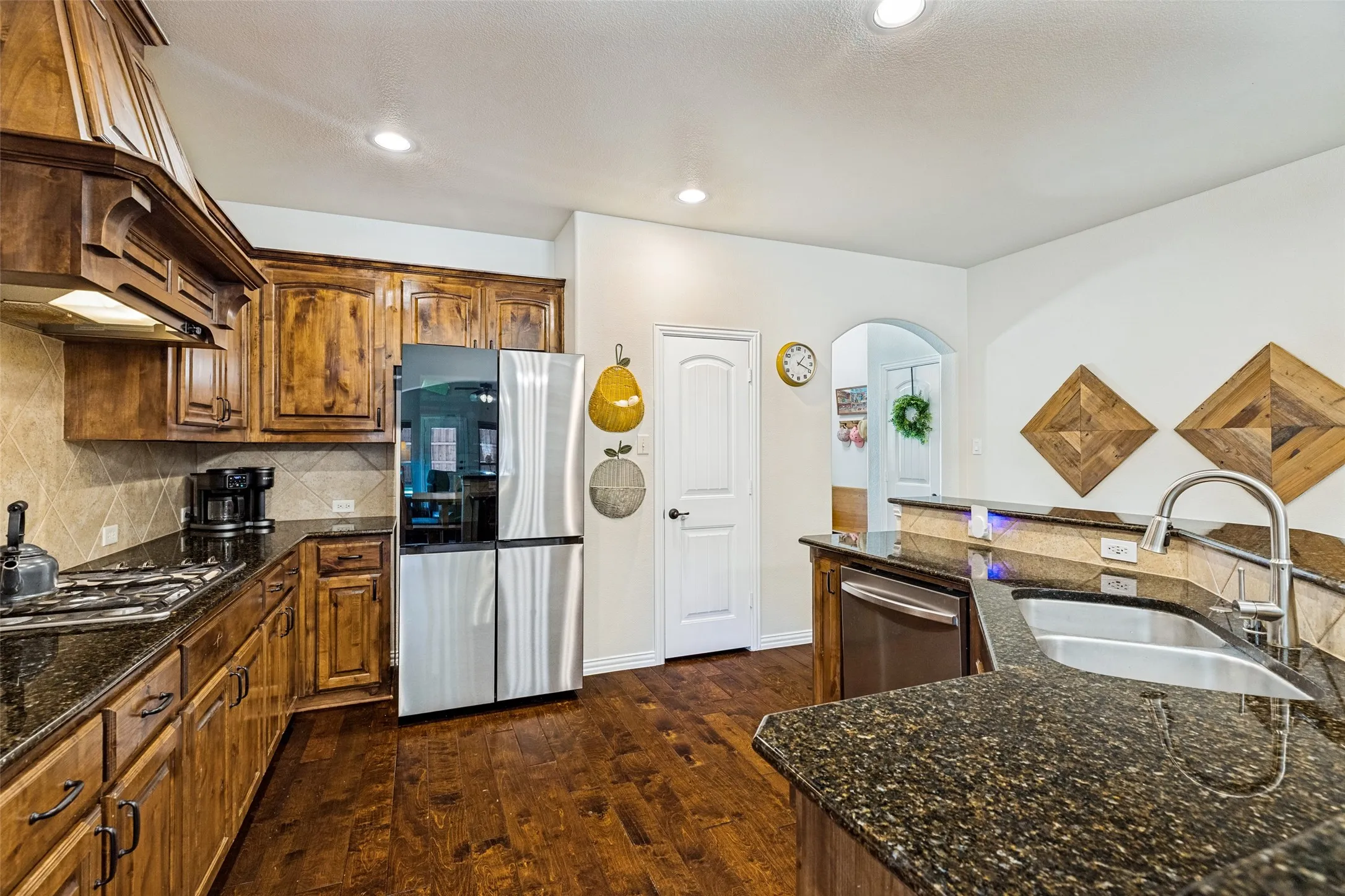 Kitchen featuring wood-finish flooring, dark wood cabinetry, stainless steel appliances, and dark speckled countertops