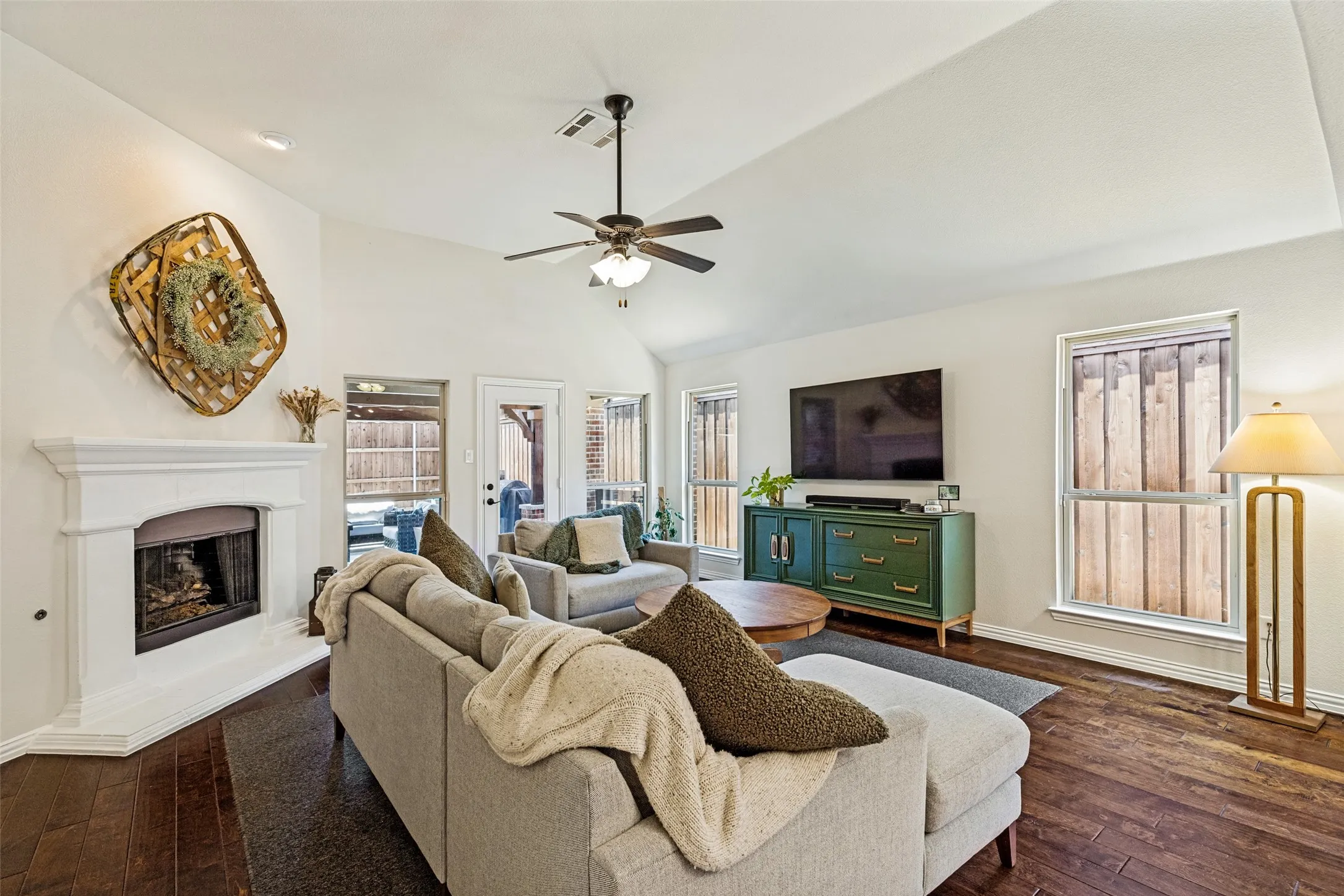 Vaulted ceiling with a ceiling fan, fireplace with a white mantel, wood-finish flooring, and an arched entryway