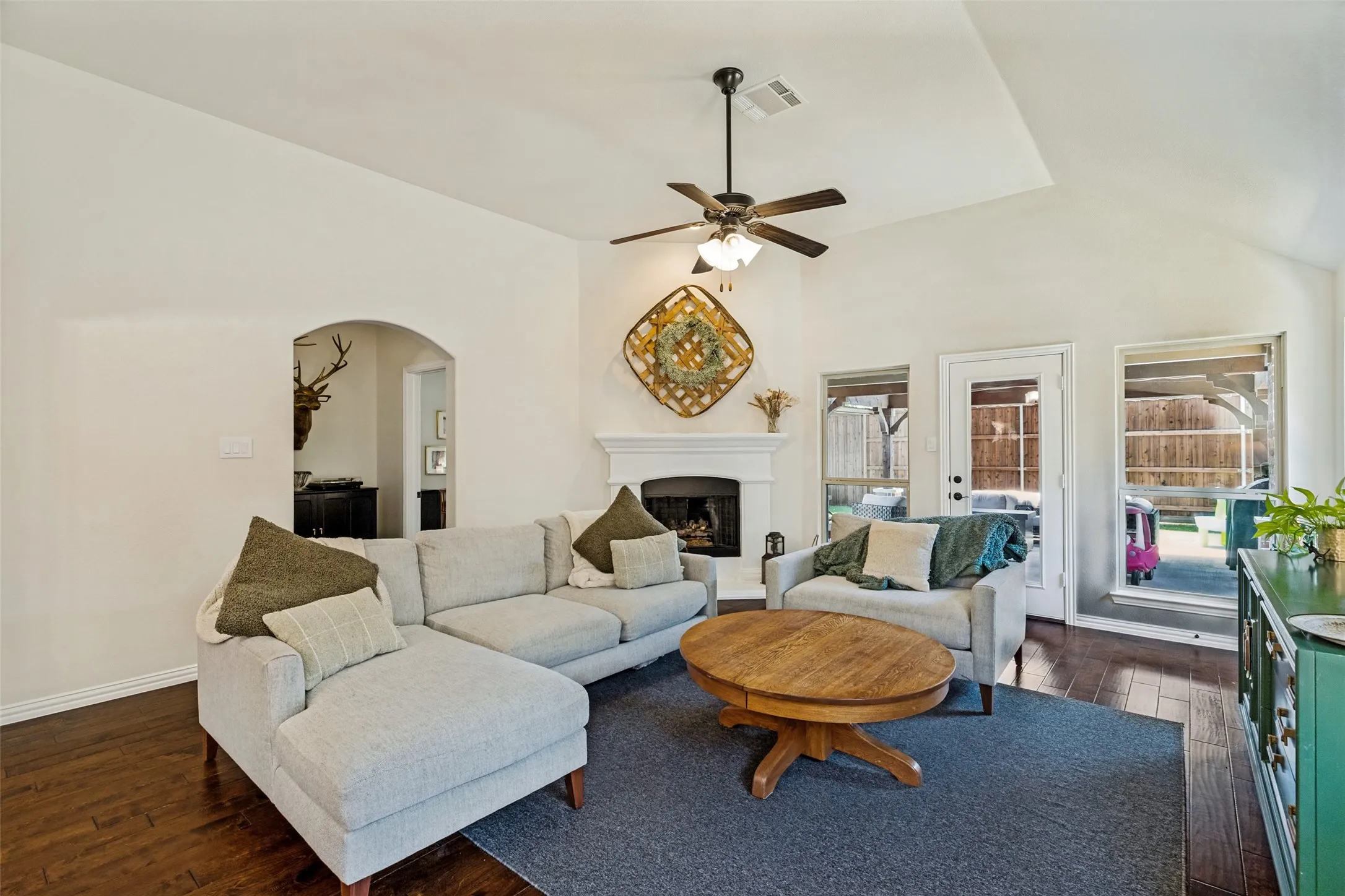Vaulted ceiling with a ceiling fan and recessed lighting, fireplace with a white mantel, arched doorways, and wood-finish flooring