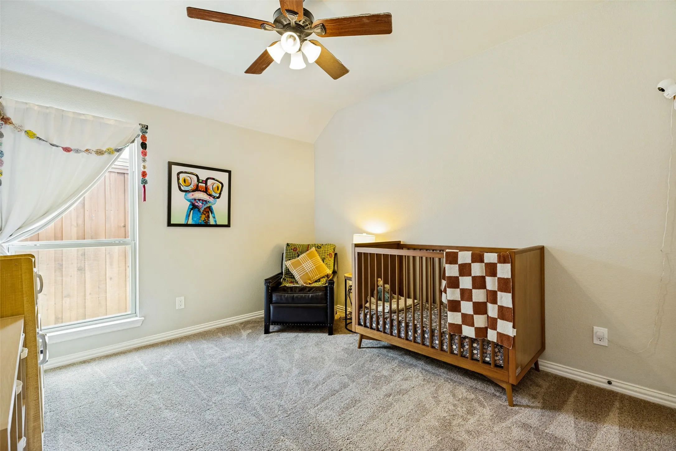 Vaulted ceiling featuring a ceiling fan, carpet flooring, and a window with wood fencing visible outside