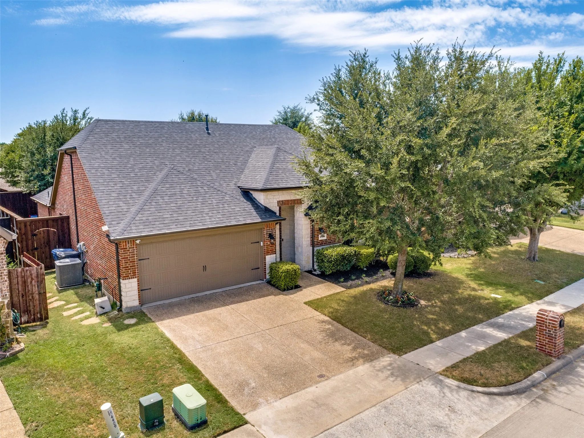 Brick and stone exterior with an attached garage, paved driveway, and mature landscaping