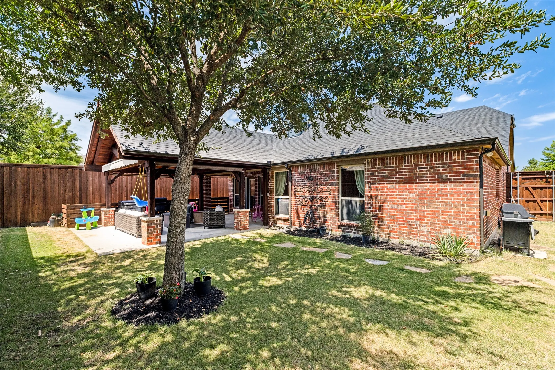 Expansive backyard featuring a covered patio, brick exterior, wood privacy fence, and mature trees