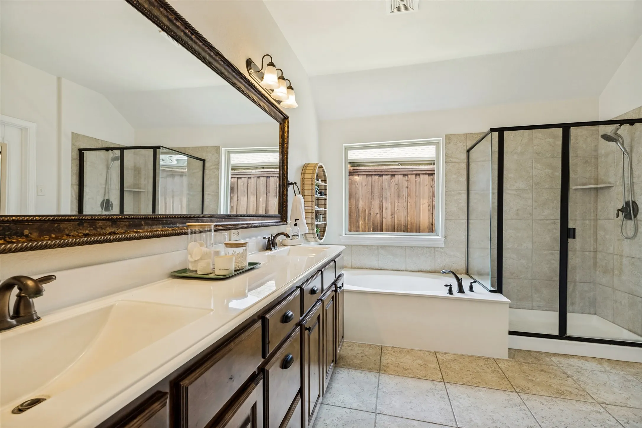 Double vanity with an expansive mirror, enclosed shower, and a soaking tub