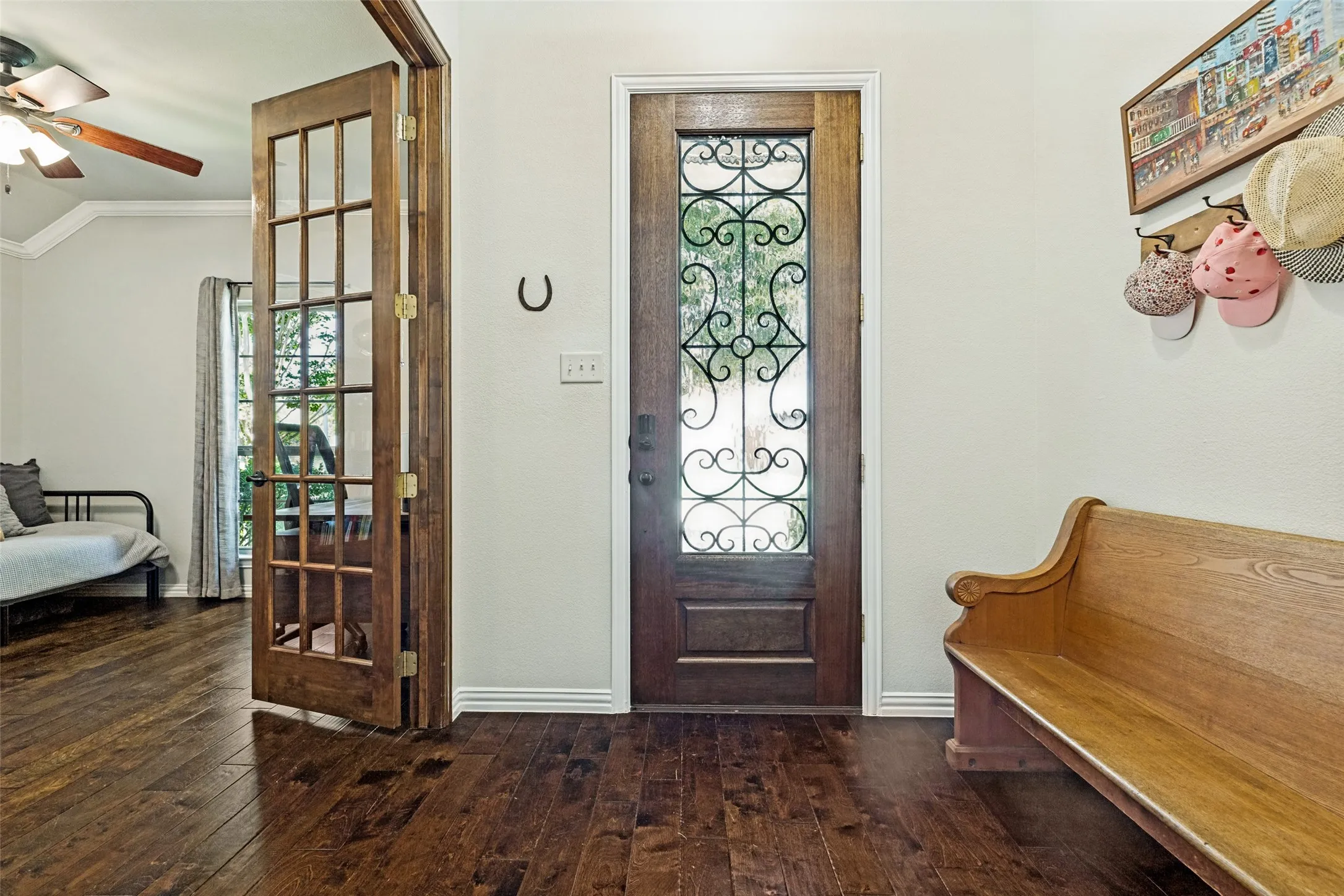 Hardwood flooring, wood-framed French doors, wood-paneled front door with decorative glass, and a ceiling fan with wood-finish blades