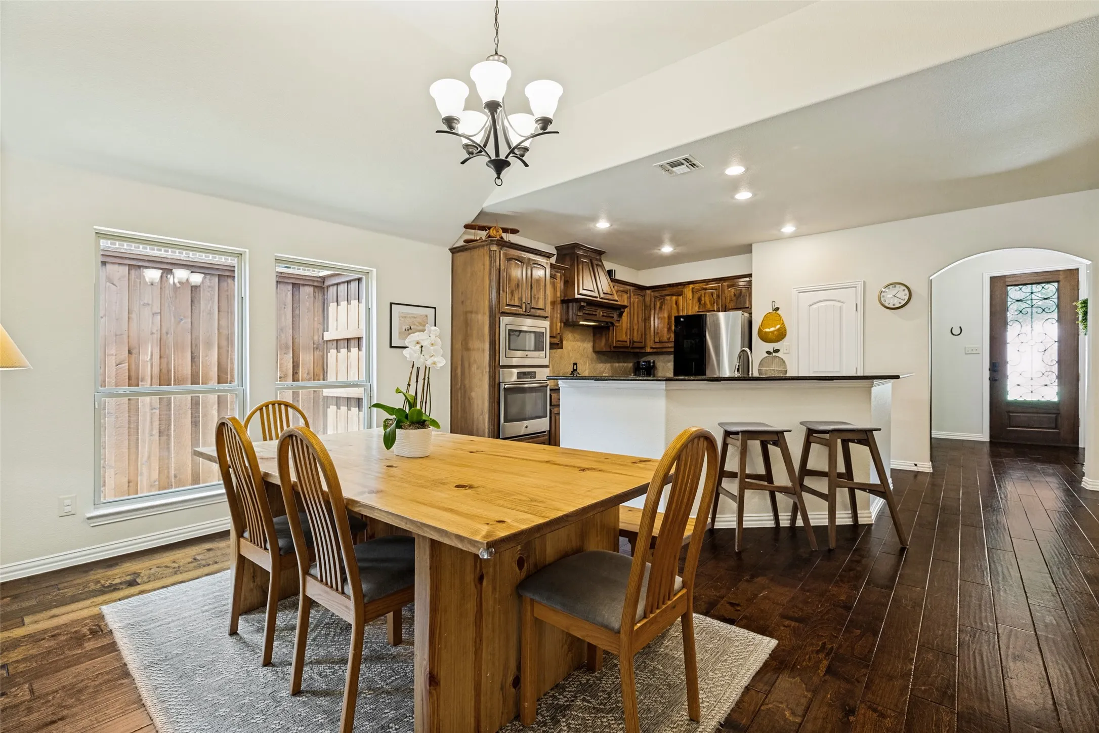 Open-concept dining area featuring dark wood-finish flooring, two windows, and an arched doorway