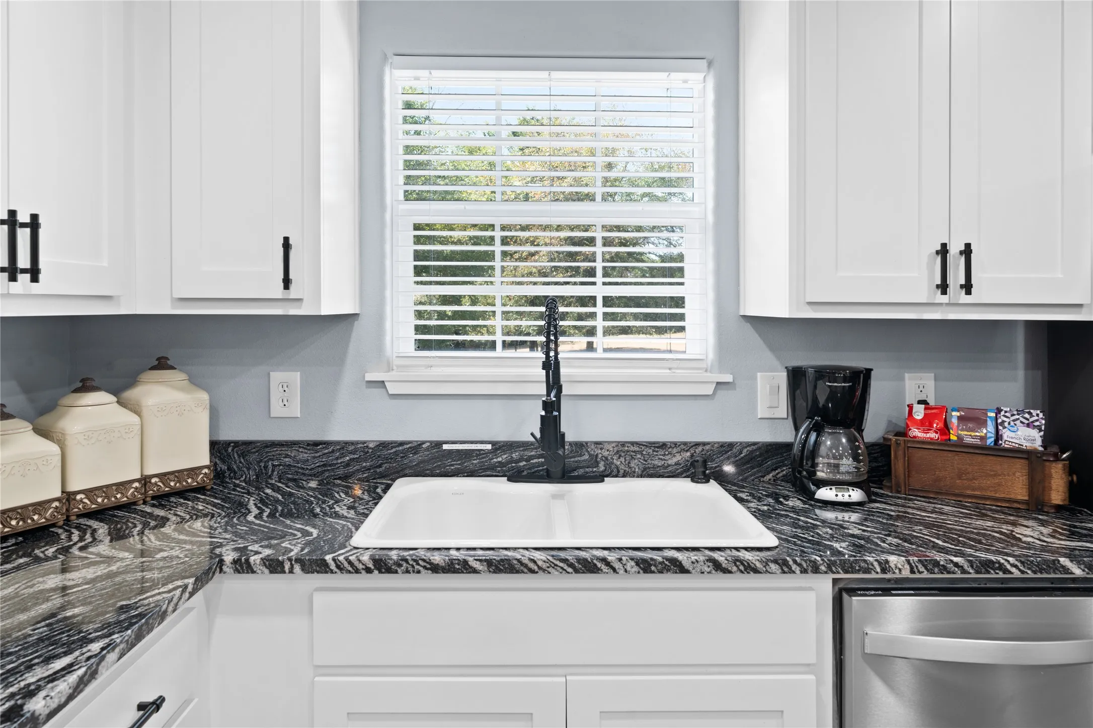 White shaker-style cabinetry with matte black hardware, dark patterned countertops, undermount sink with a black faucet, and a stainless steel appliance