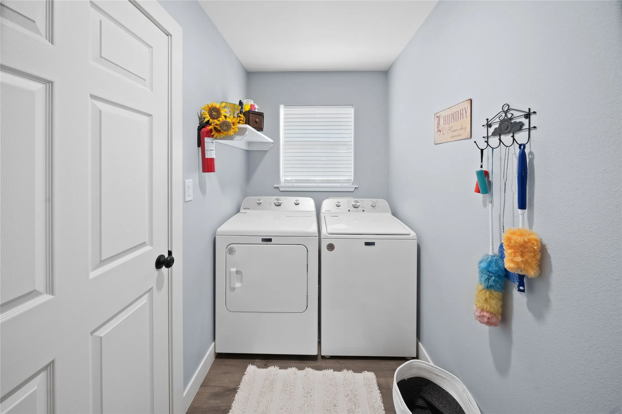 Laundry area featuring wood-finish flooring, a window with blinds, and white painted walls