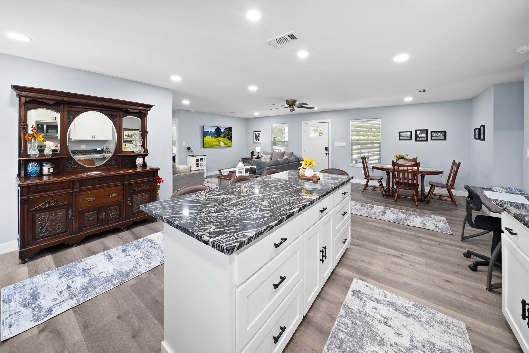 Open-concept living space featuring wood-finish flooring, recessed lighting, and a kitchen island with a dark patterned countertop and white cabinetry