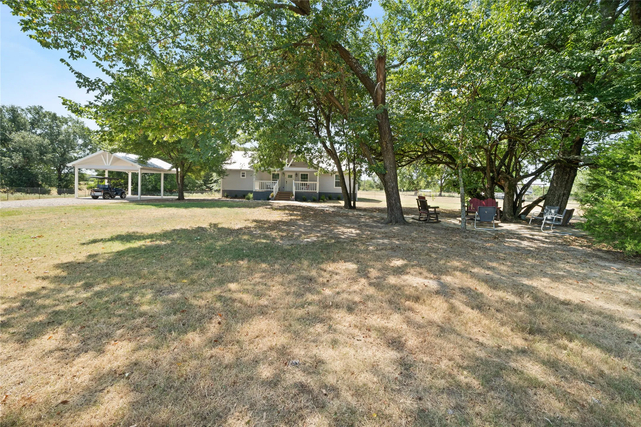 Expansive shaded yard featuring mature trees and a two-car detached carport with elect