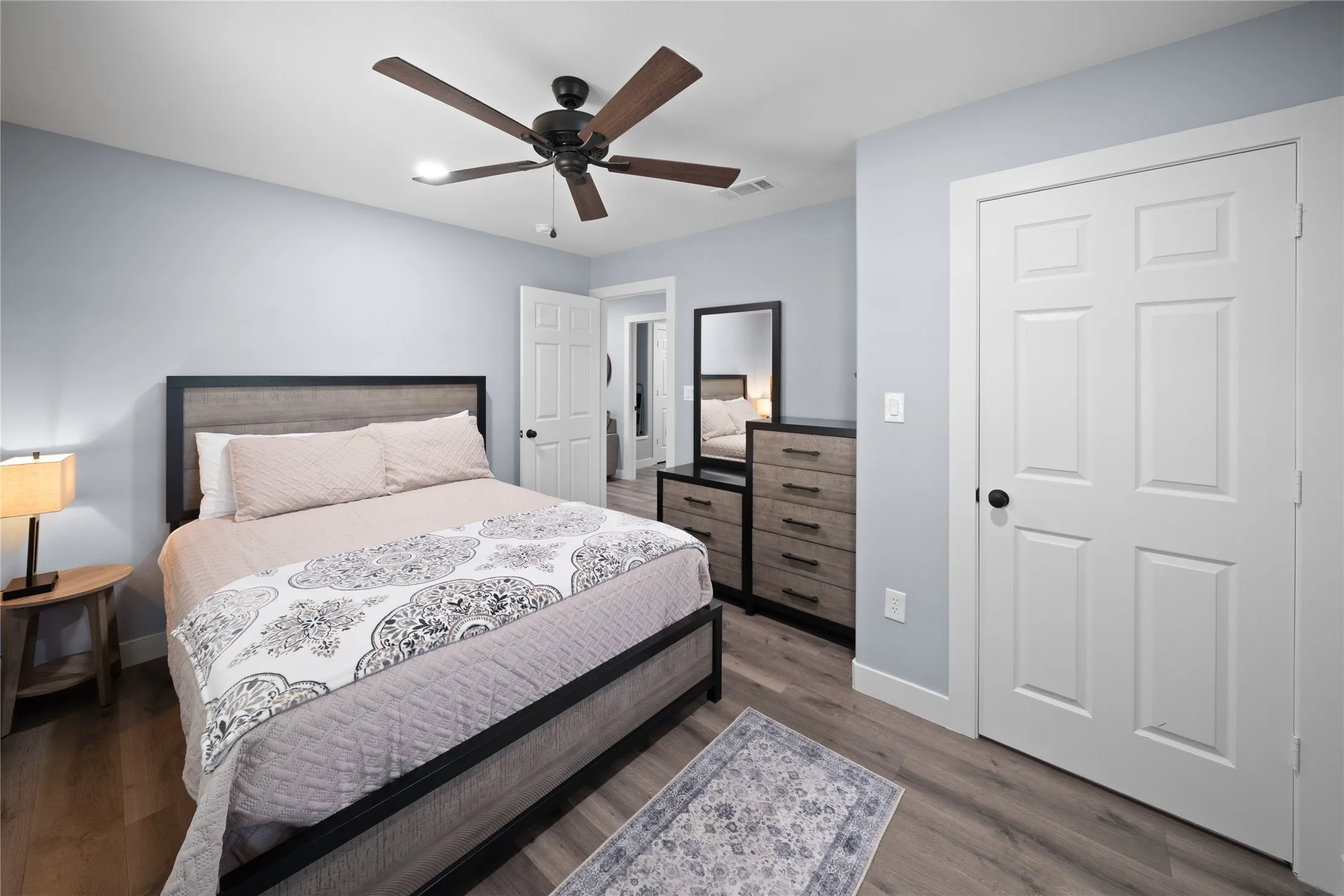 Wood-finish flooring, ceiling fan with light fixture, light gray walls, and white paneled doors