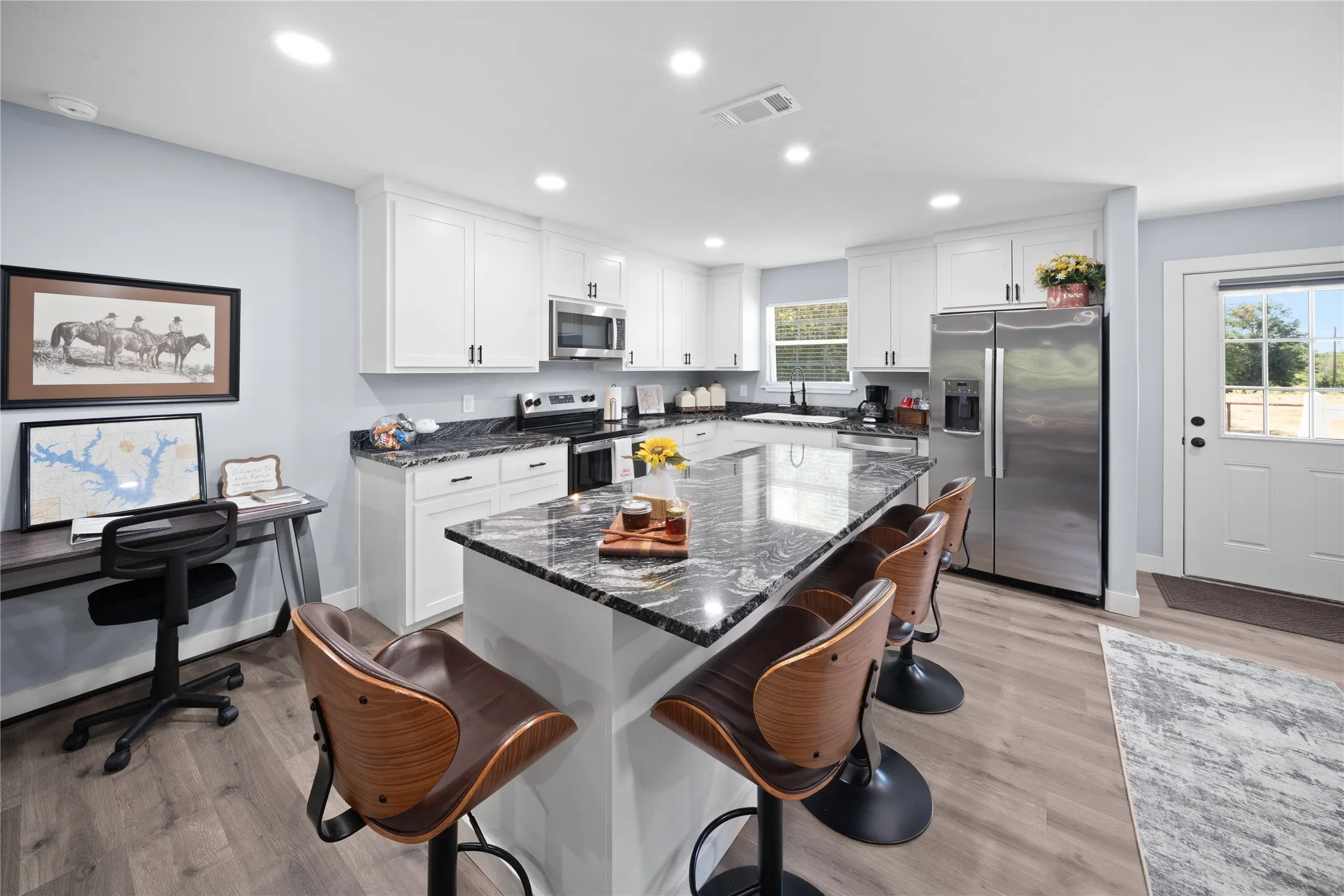 Modern kitchen with white cabinetry, stainless steel appliances, a large island with seating, dark stone countertops, and wood-finish flooring
