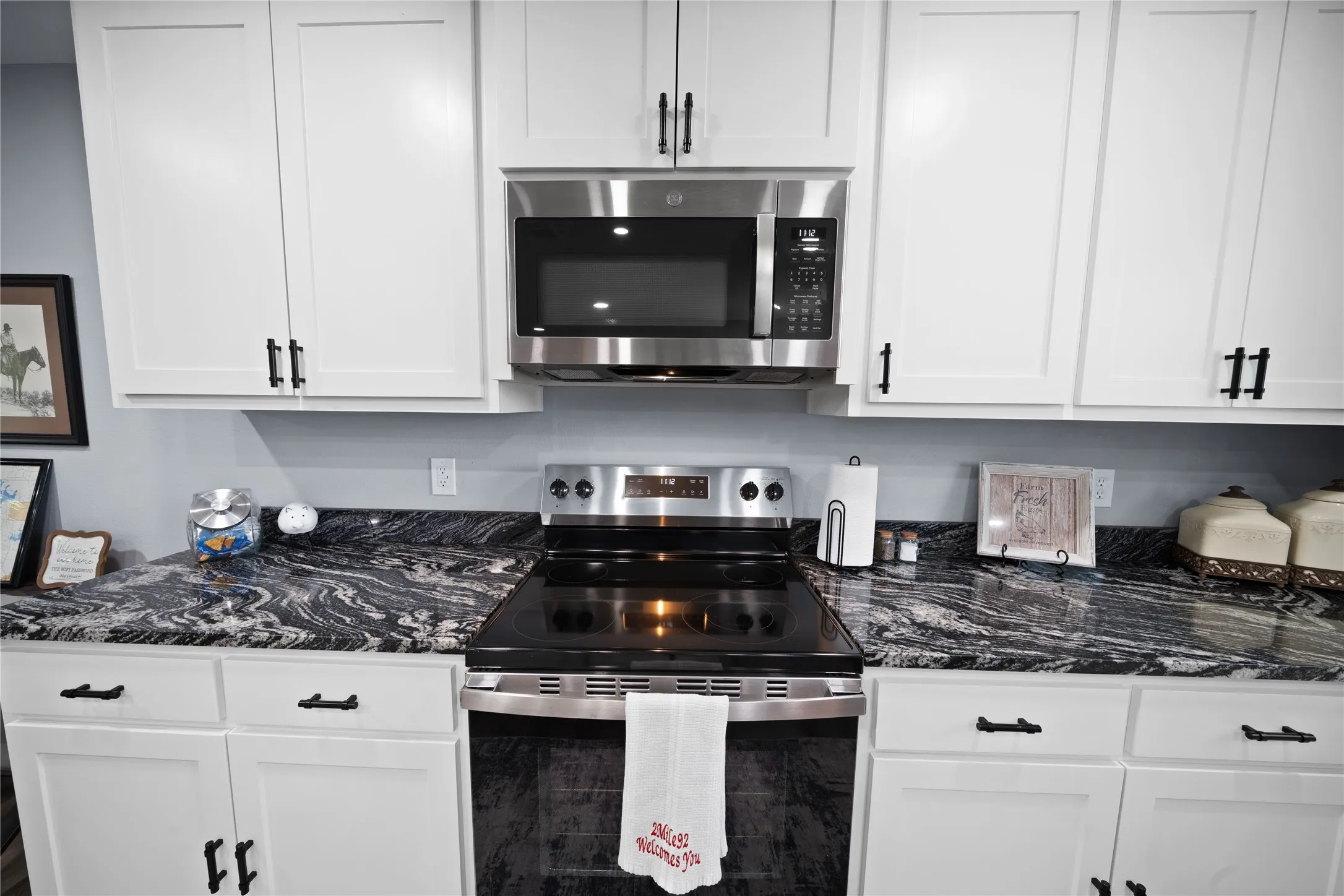 White cabinetry with dark hardware, stainless steel appliances, dark patterned countertops, and a built-in microwave