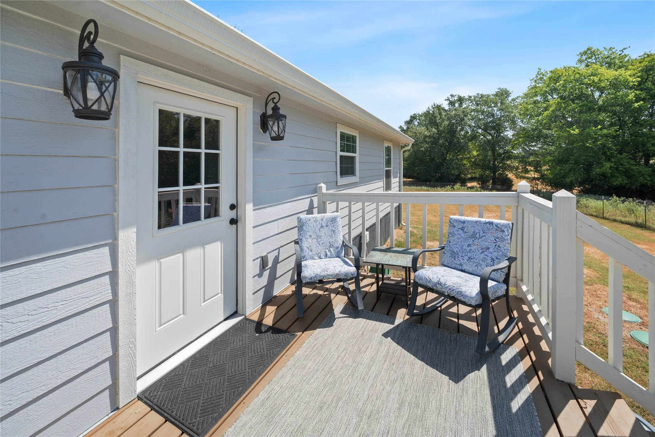 Rear wood deck with white railing, light-colored horizontal siding, and multiple exterior light fixtures